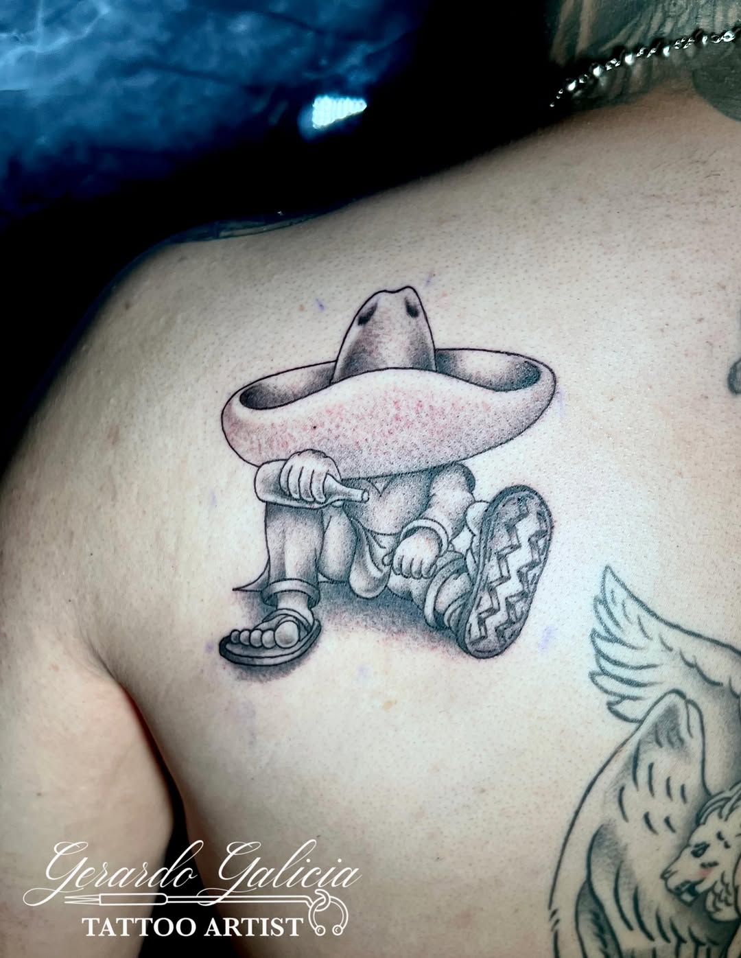 Man in sombrero with bottle tattoo on the shoulder by Gerardo Galicia, New York, New York