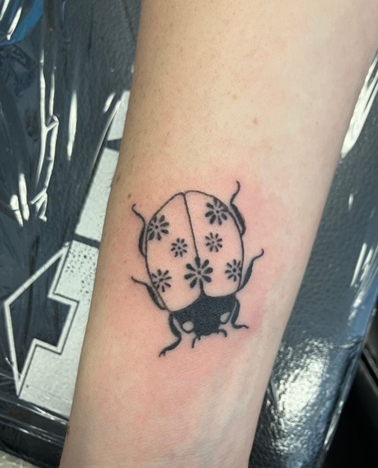 Ladybug with flowers fine line tattoo on the forearm by Bryant Johnson