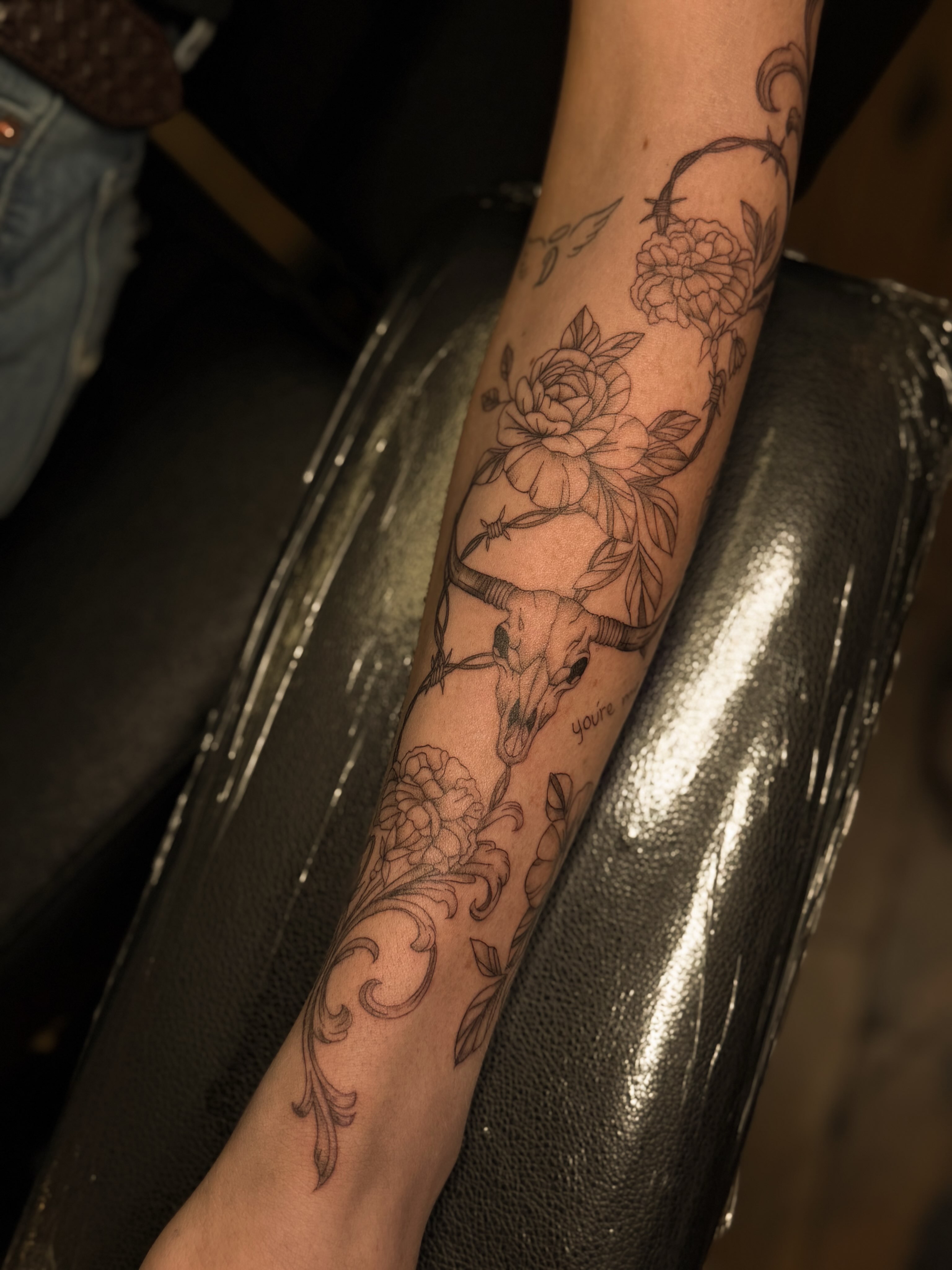 Floral and skull design black and grey tattoo on the forearm by Courtney