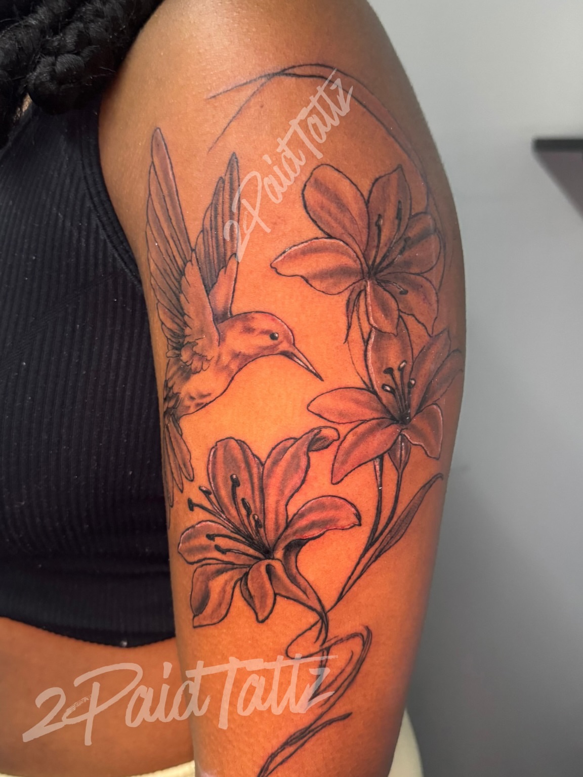 Lilies and hummingbird black and grey tattoo on the upper arm by 2PaidTattz