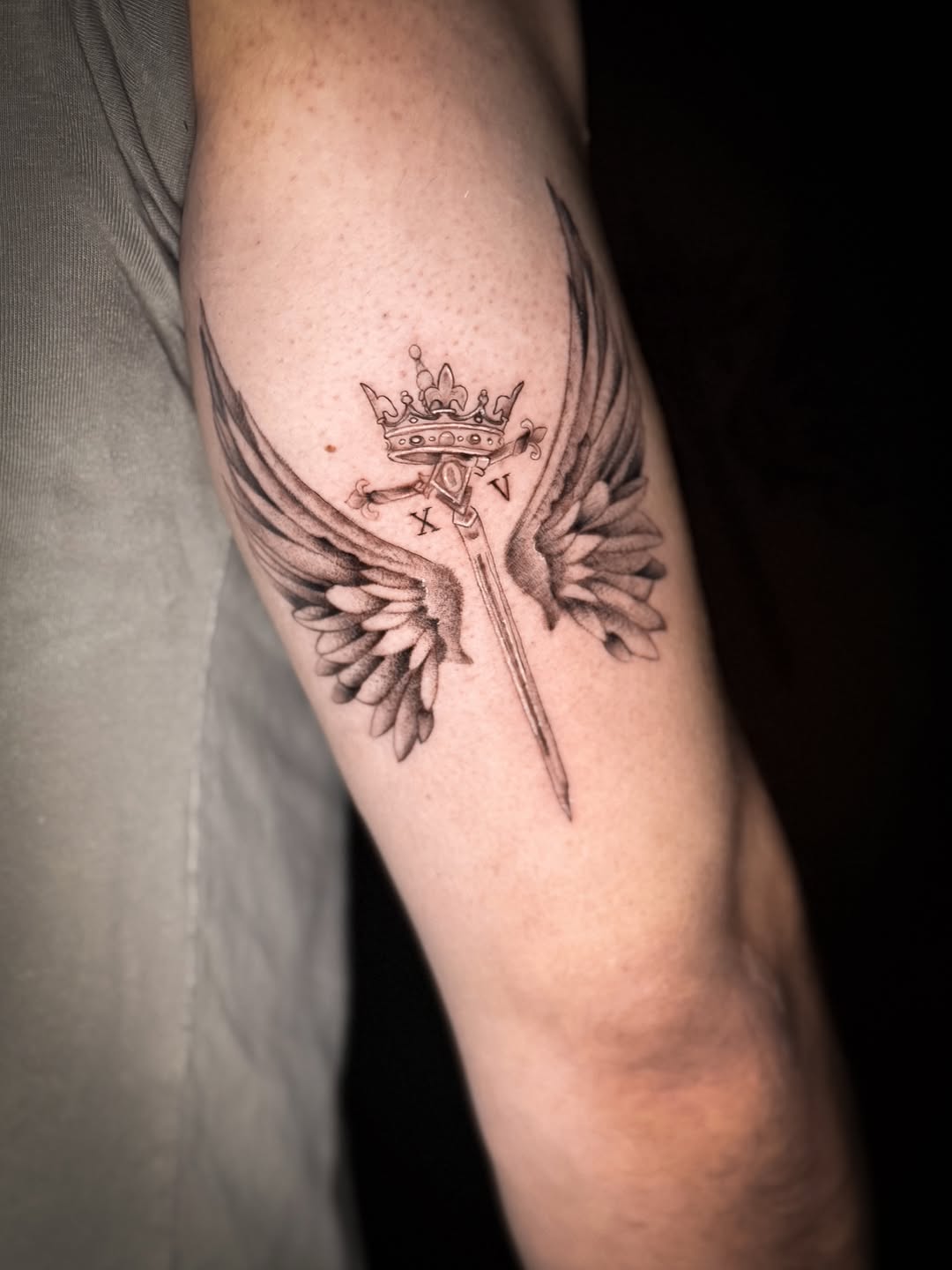 Sword with crown and wings realism tattoo on the forearm by Jennifer Ramirez