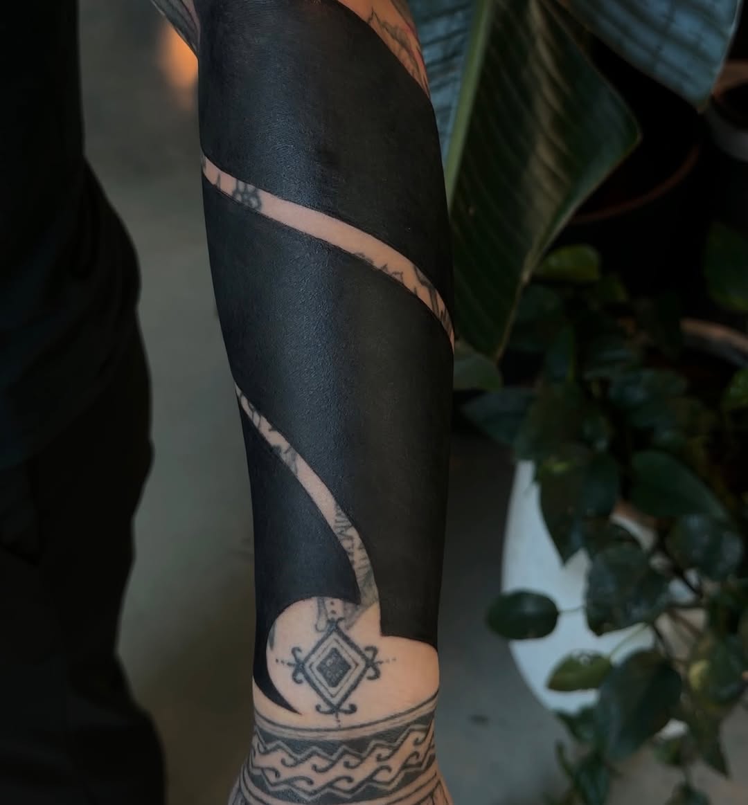 Abstract black fill with geometric accents tribal tattoo on the forearm by Rachel