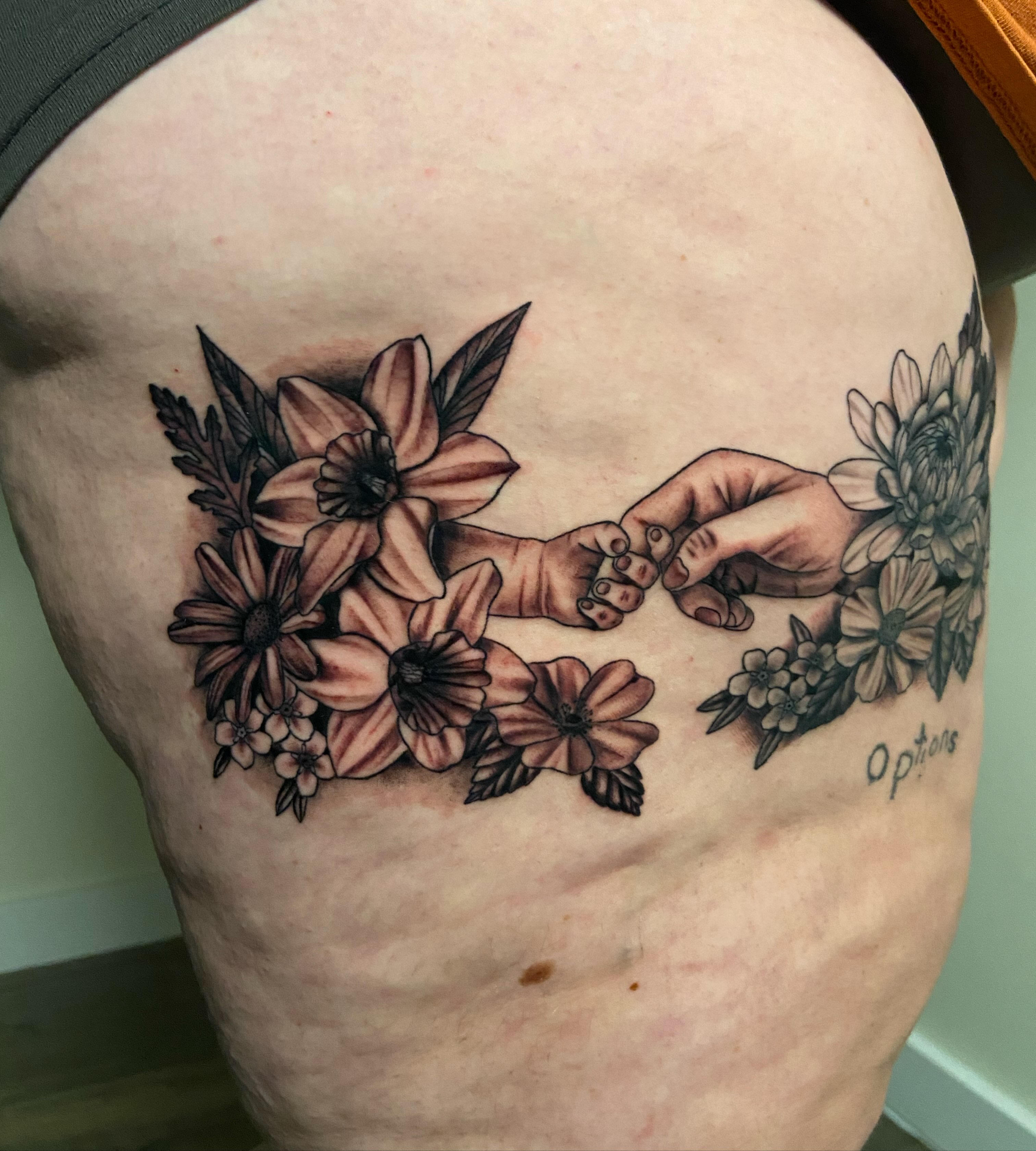 Baby feet and hands black and grey tattoo on the thigh by Ezra Gonda