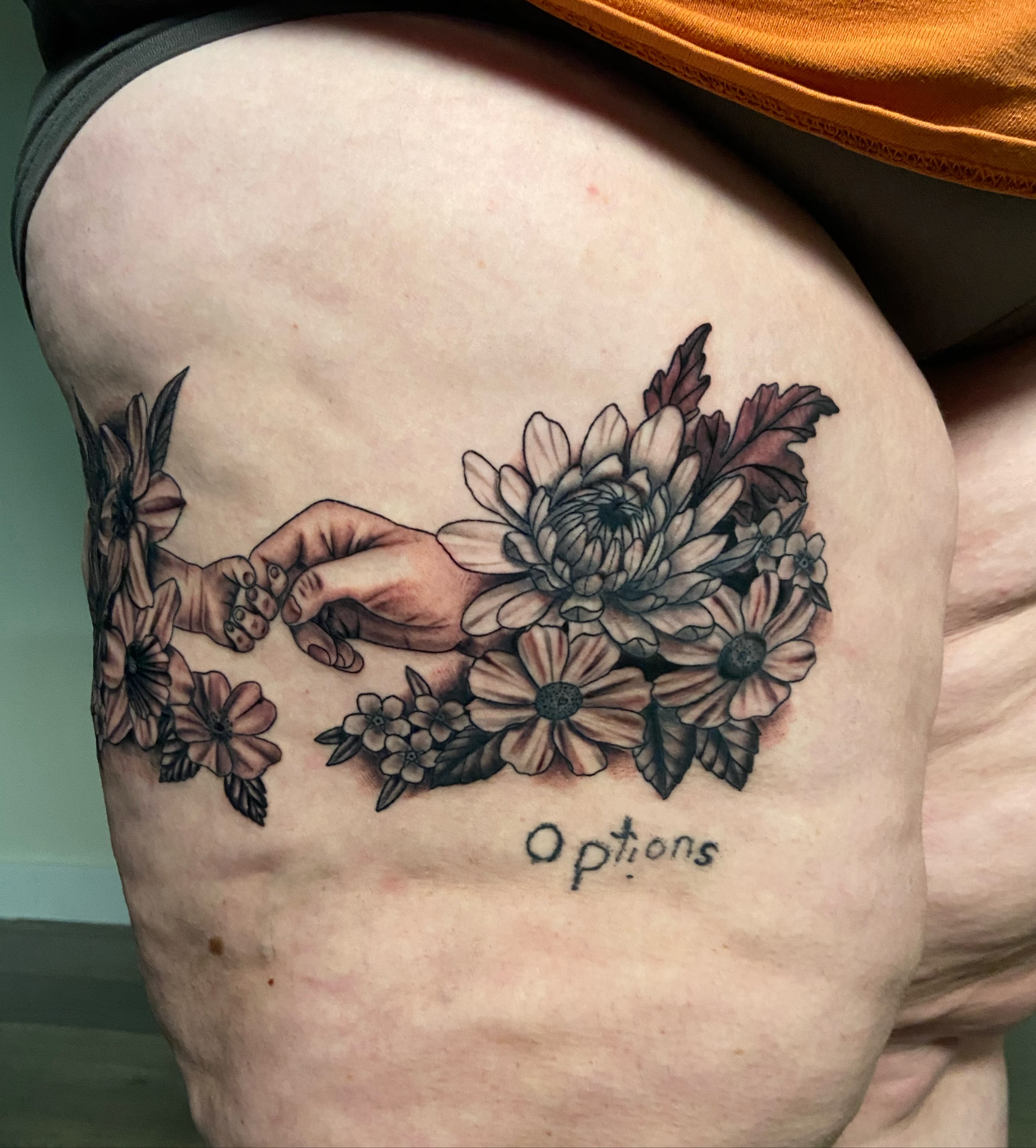 Touching hands with flowers realism tattoo on the thigh by Ezra Gonda