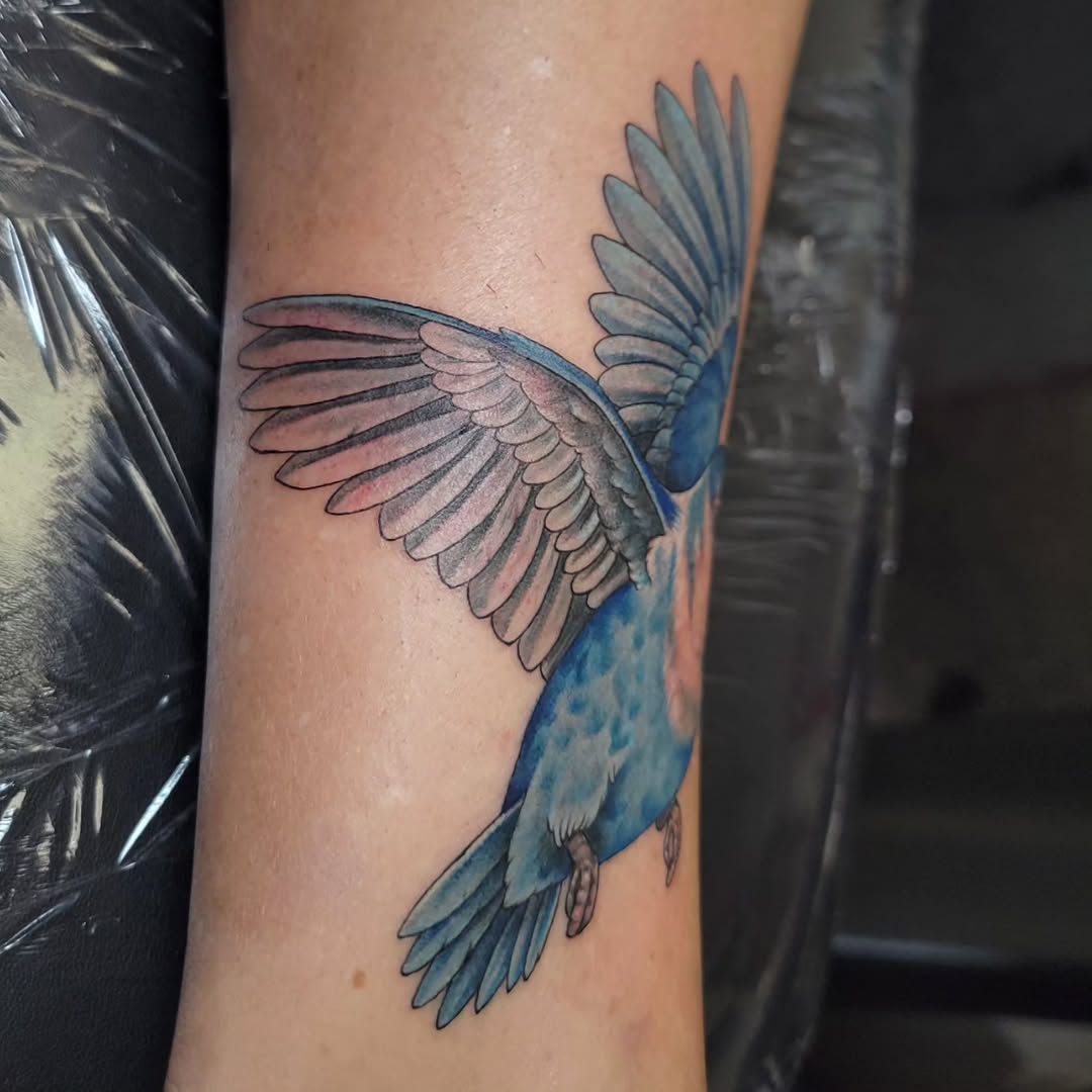 Blue bird with wings spread watercolor tattoo on the forearm by Marina Cobb