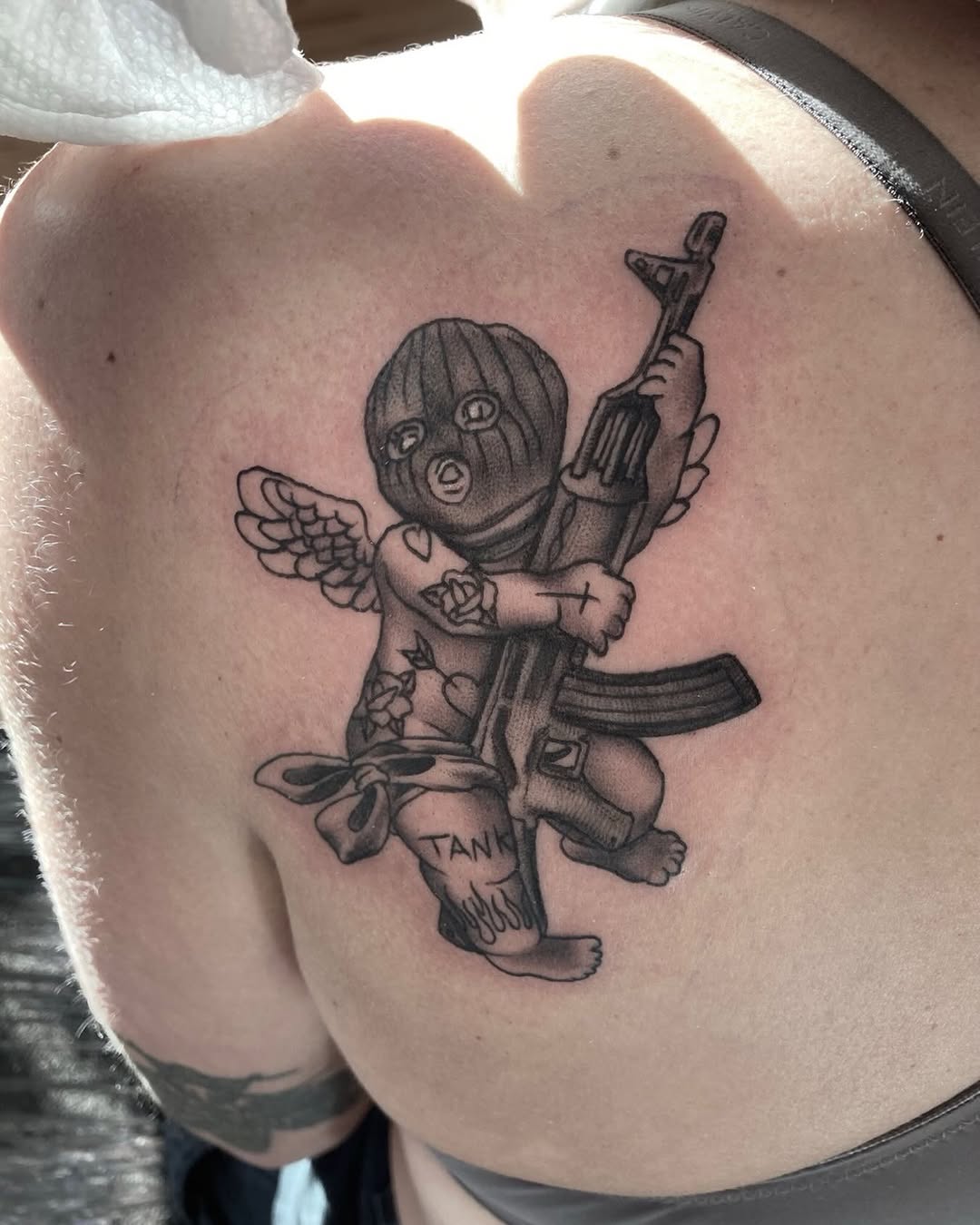 Cherub with ski mask and rifle ignorant tattoo on the shoulder by Jixonai C