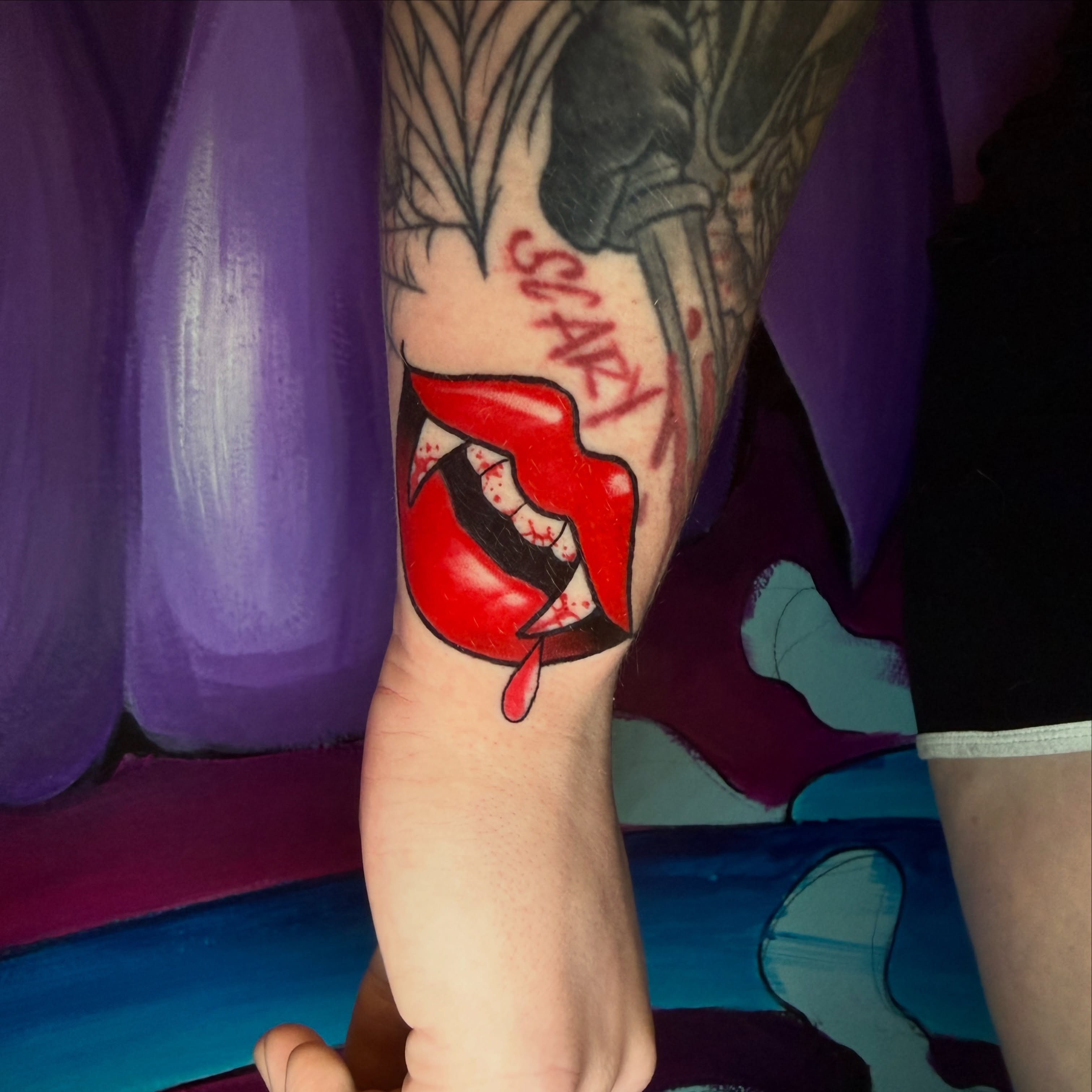 Red lips with fangs realism tattoo on the forearm by Rebecca Preble