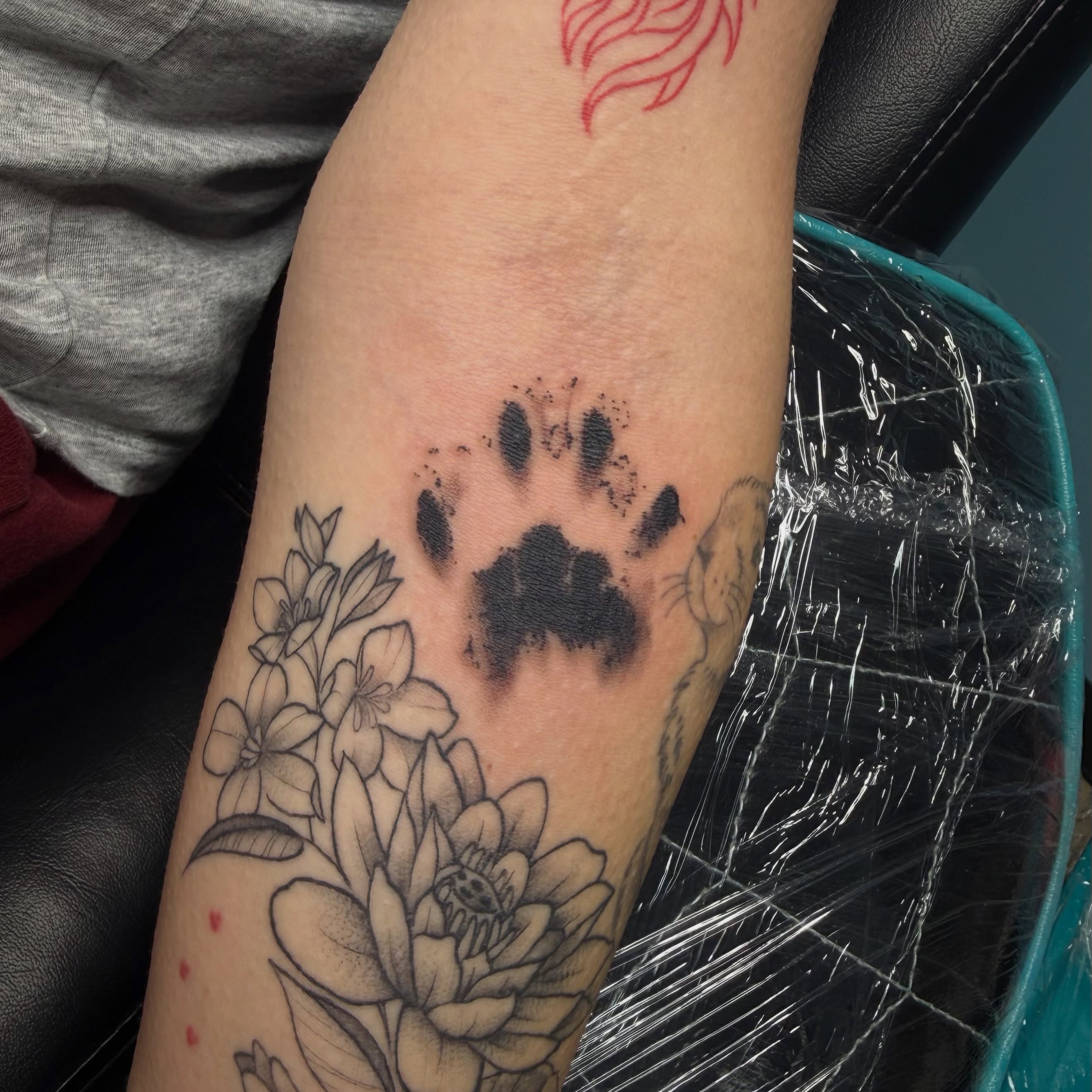 Paw print with flowers black and grey tattoo on the forearm by Rebecca Preble