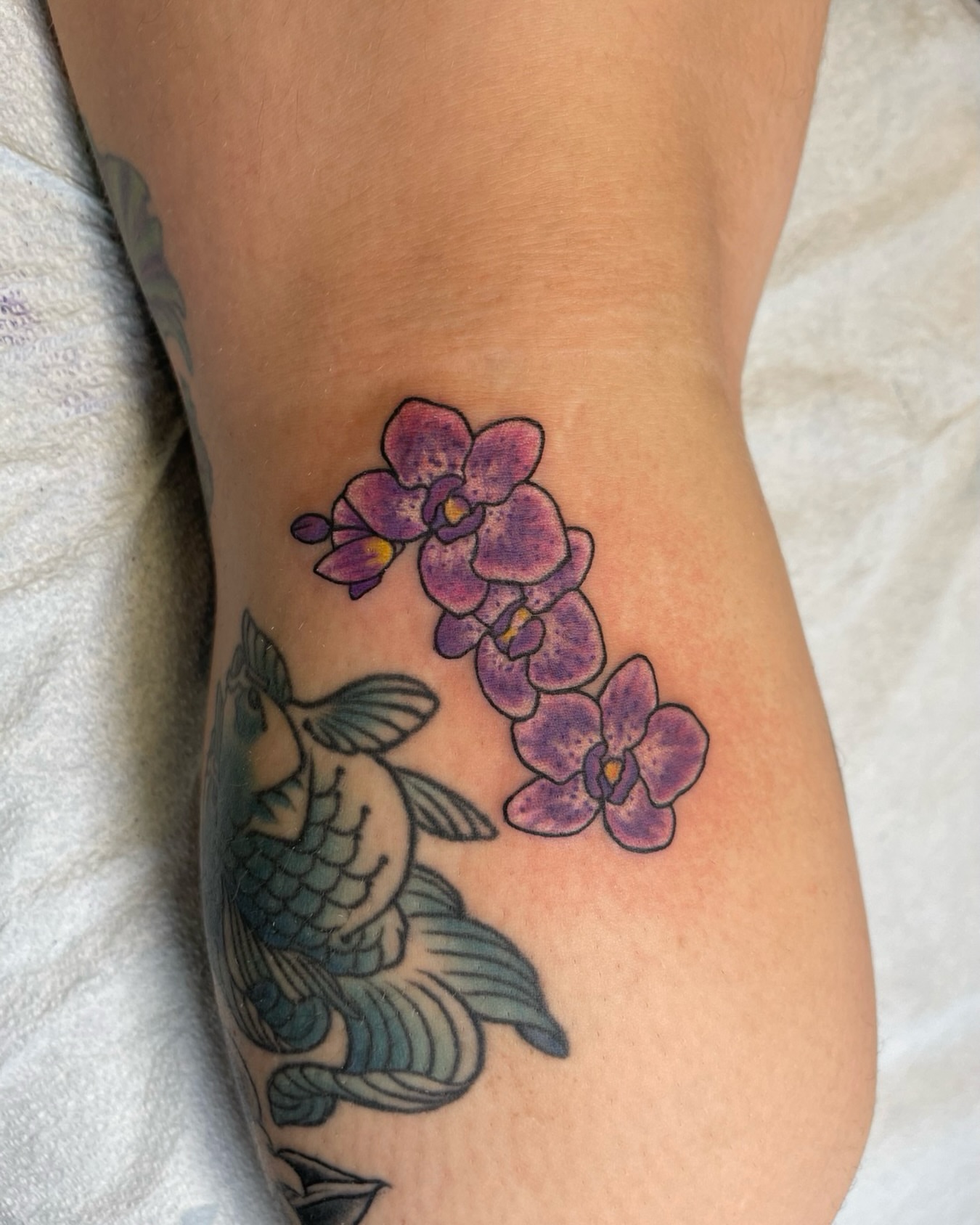 Orchids and fish new school tattoo on the forearm by Ashley Antolin