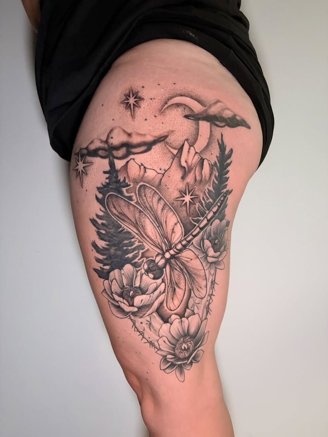 Dragonfly with landscape and flowers fine line tattoo on the thigh by Kenzie Mecham-Cunningham