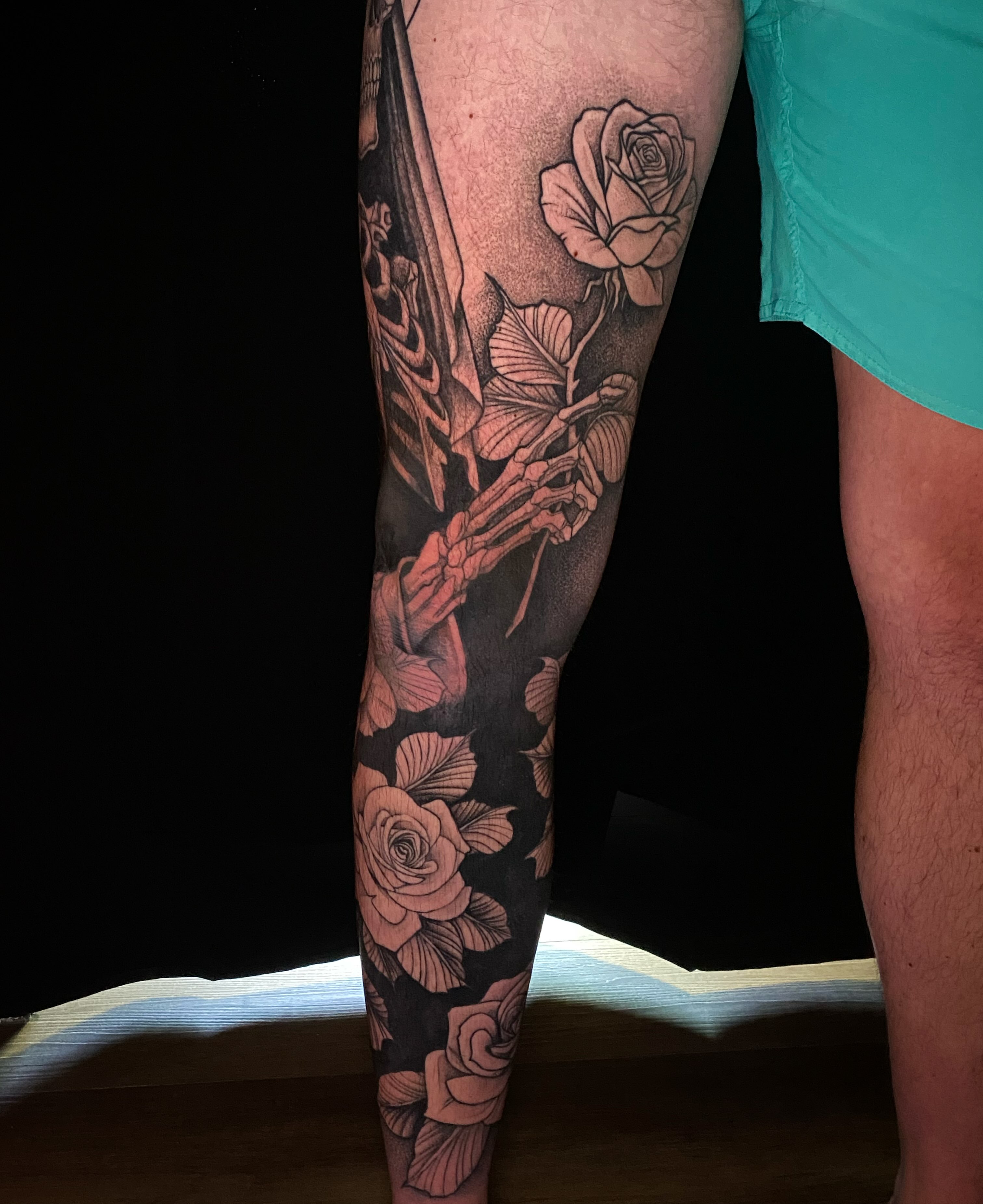 Skeleton with roses black and grey tattoo on the leg by Casey Dohner