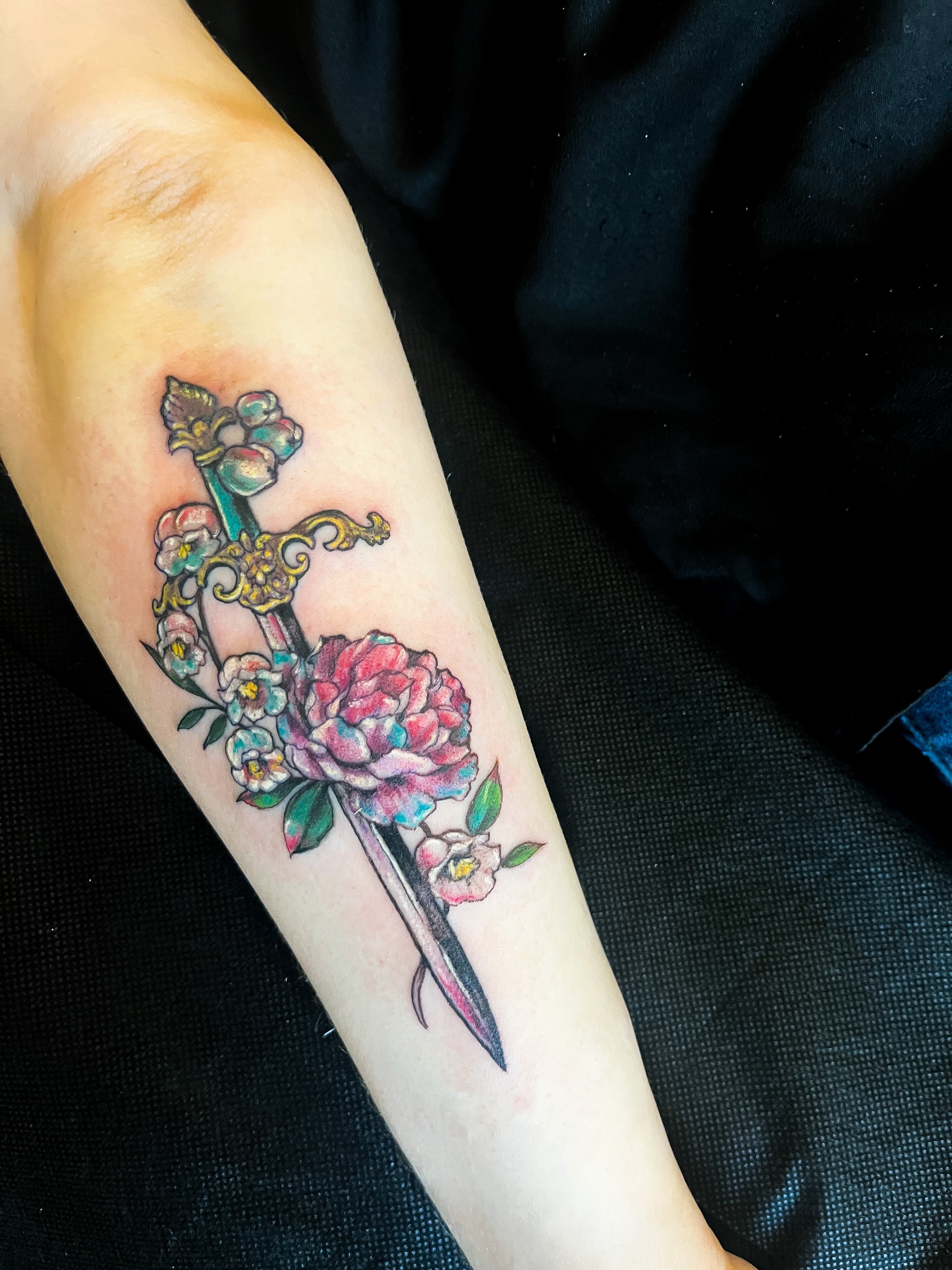 Sword and flowers American traditional tattoo on the forearm by Janelle Cuba