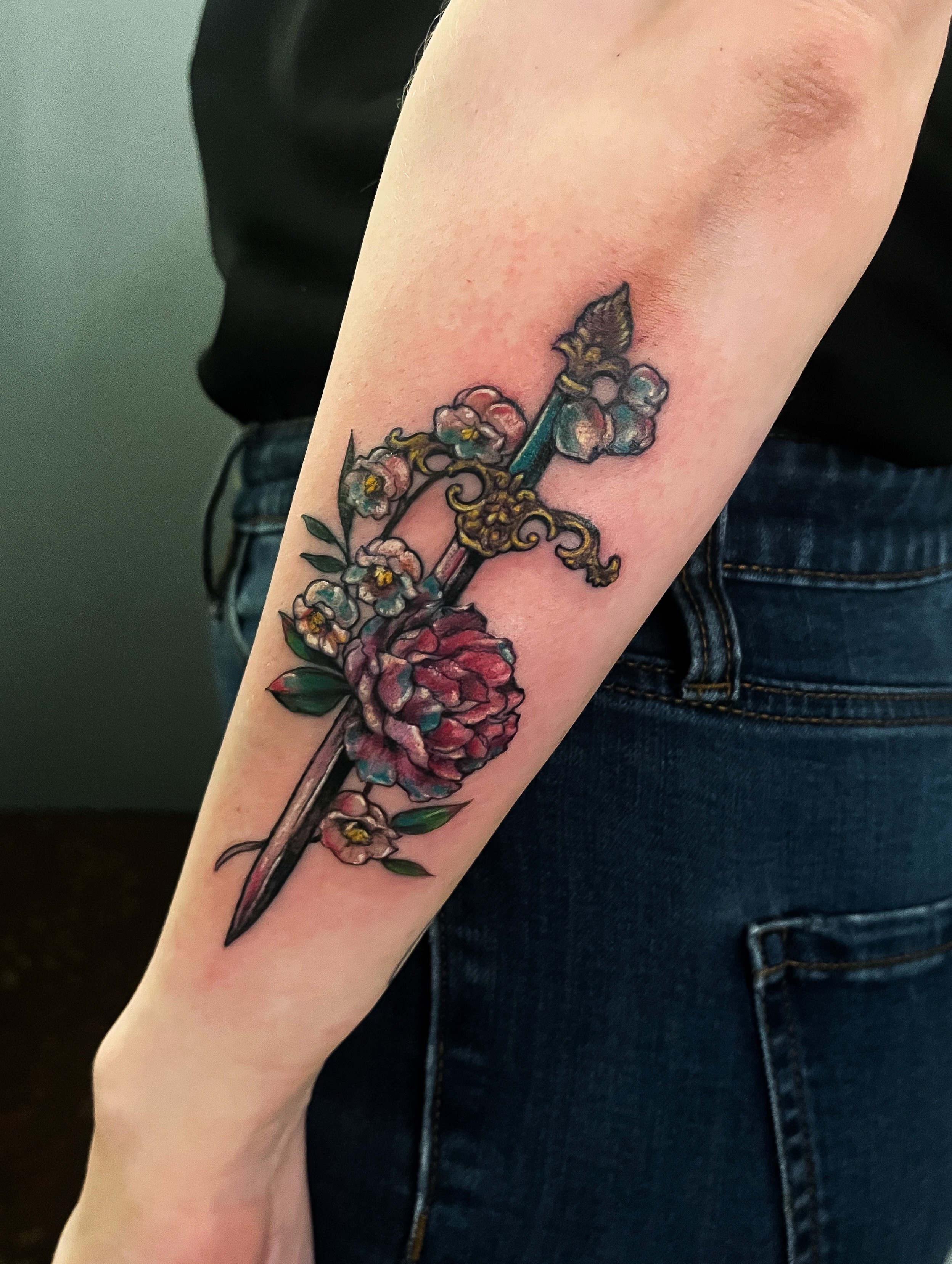 Cross with floral decoration new school tattoo on the forearm by Janelle Cuba