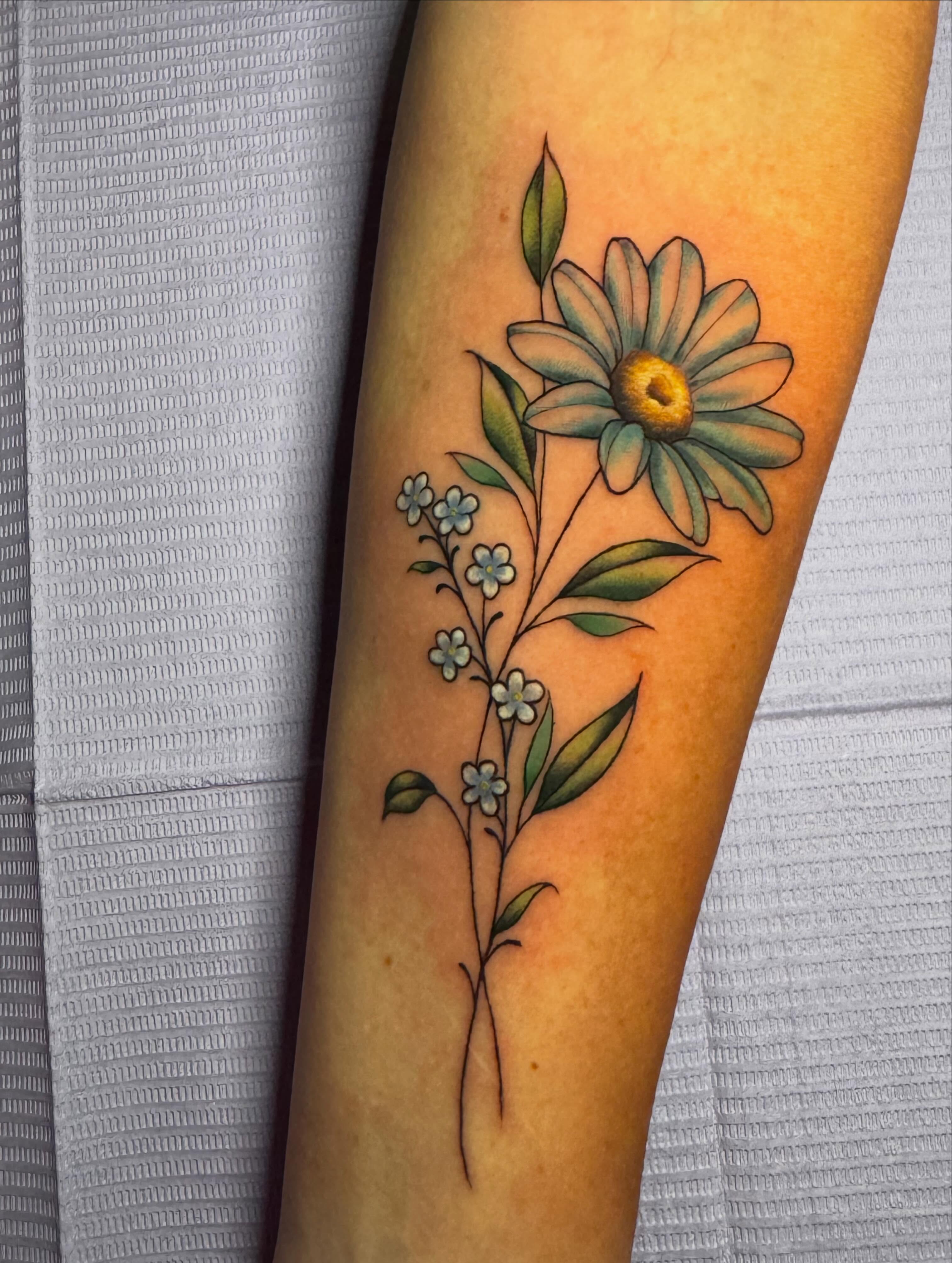 Daisy and forget-me-nots realism tattoo on the forearm by Patience Moore