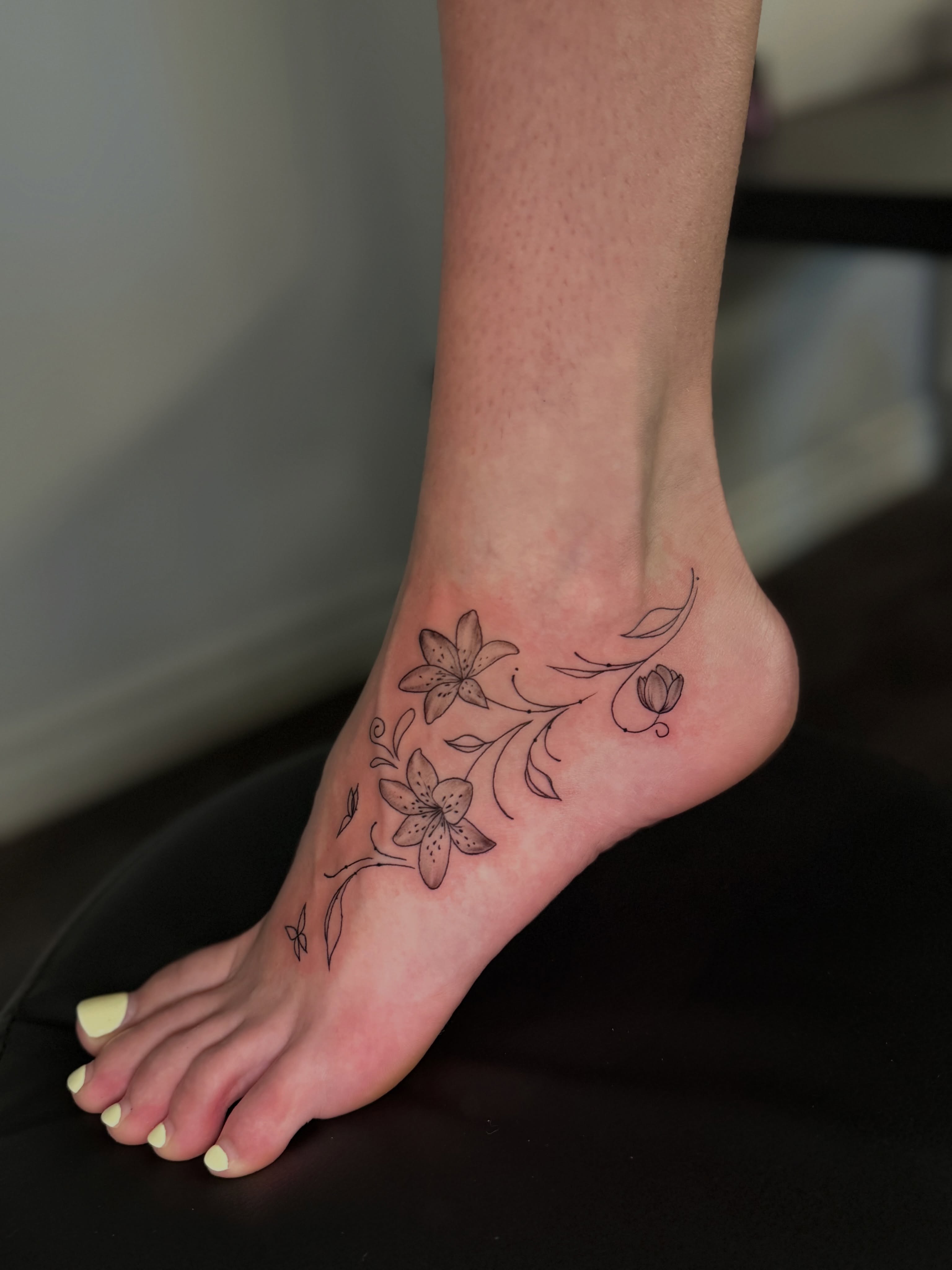 Lily flowers black and grey tattoo on the foot by Mandy Kaur