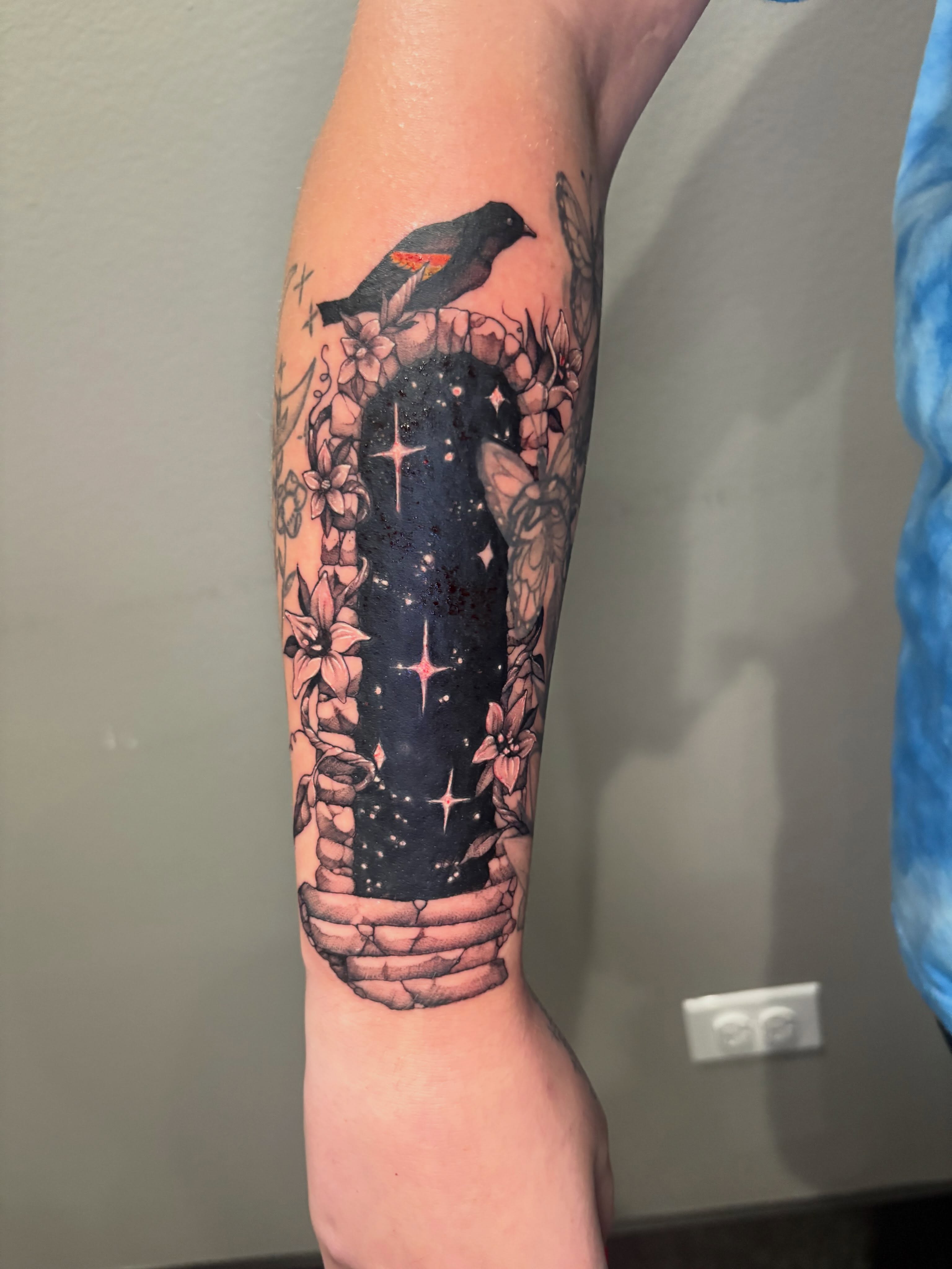 Night sky with bird and flowers realism tattoo on the forearm by Eddie Wolfe