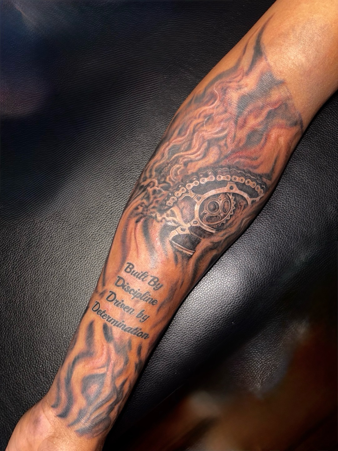 Flame and gear black and grey tattoo on the forearm by K.L Tattoo Uptown