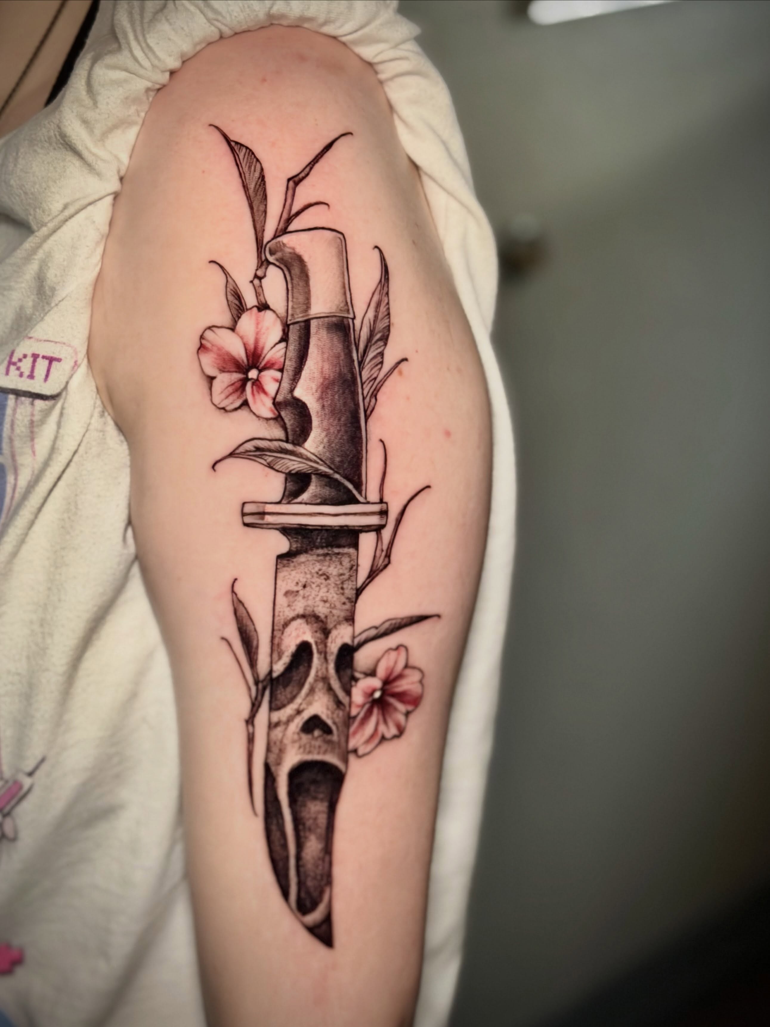 Knife with skull and flowers realism tattoo on the forearm by Adam Newton