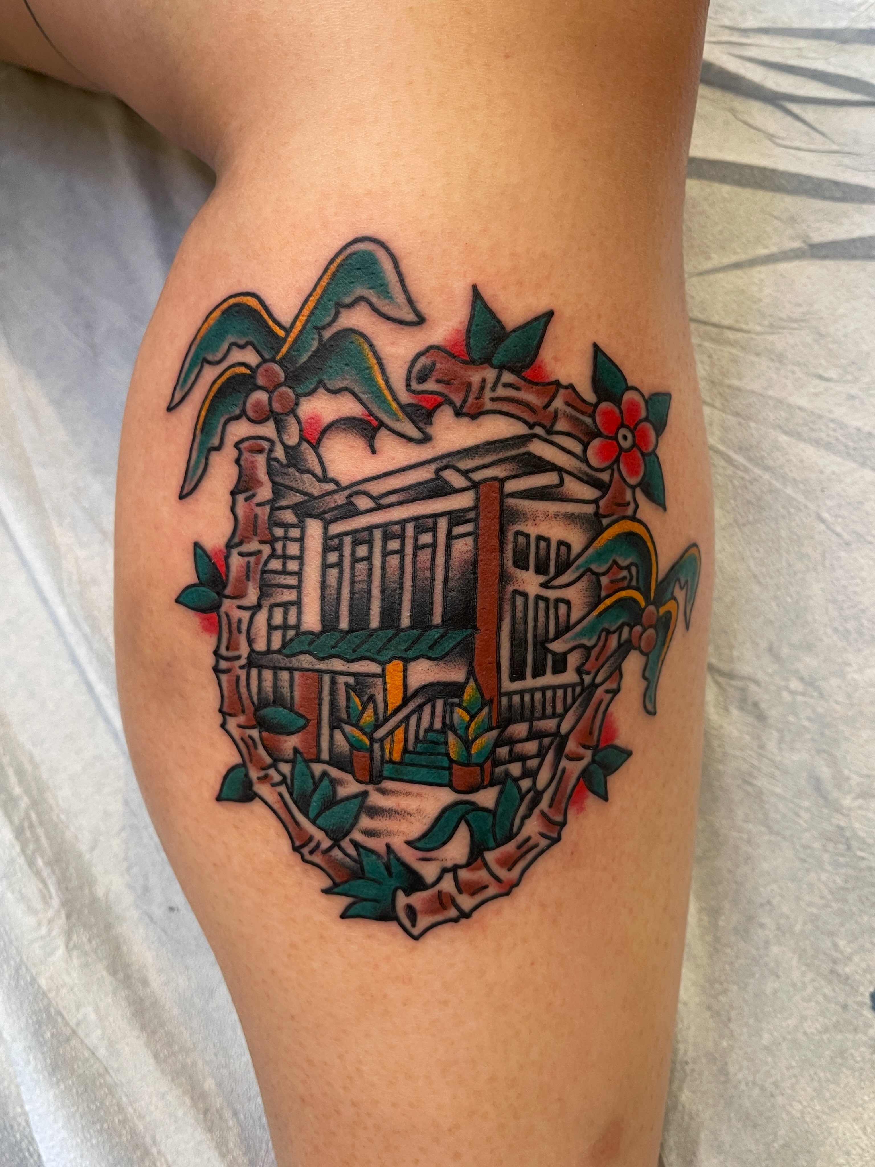 Building with tropical foliage American traditional tattoo on the thigh by Spencer Reisbeck