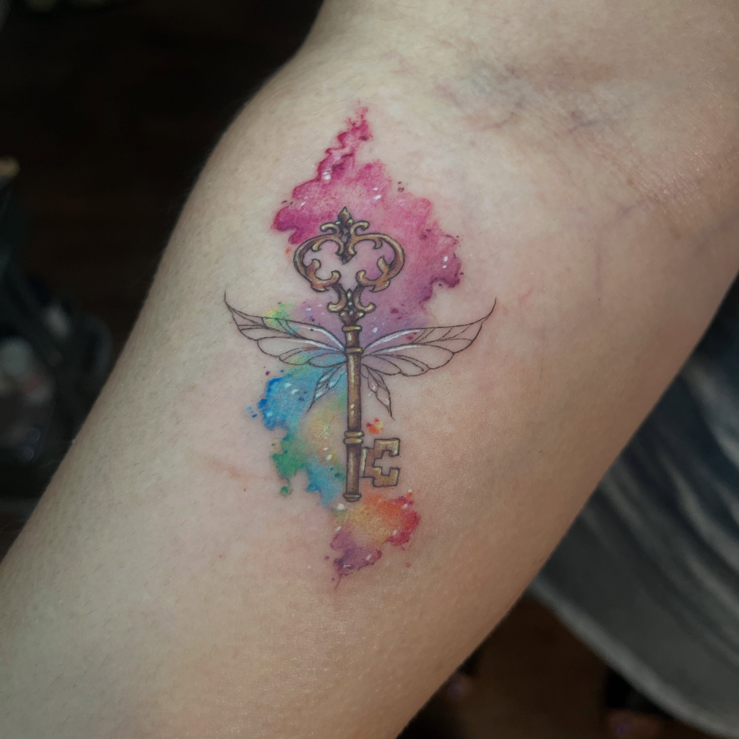 Key with wings watercolor tattoo on the forearm by SJ