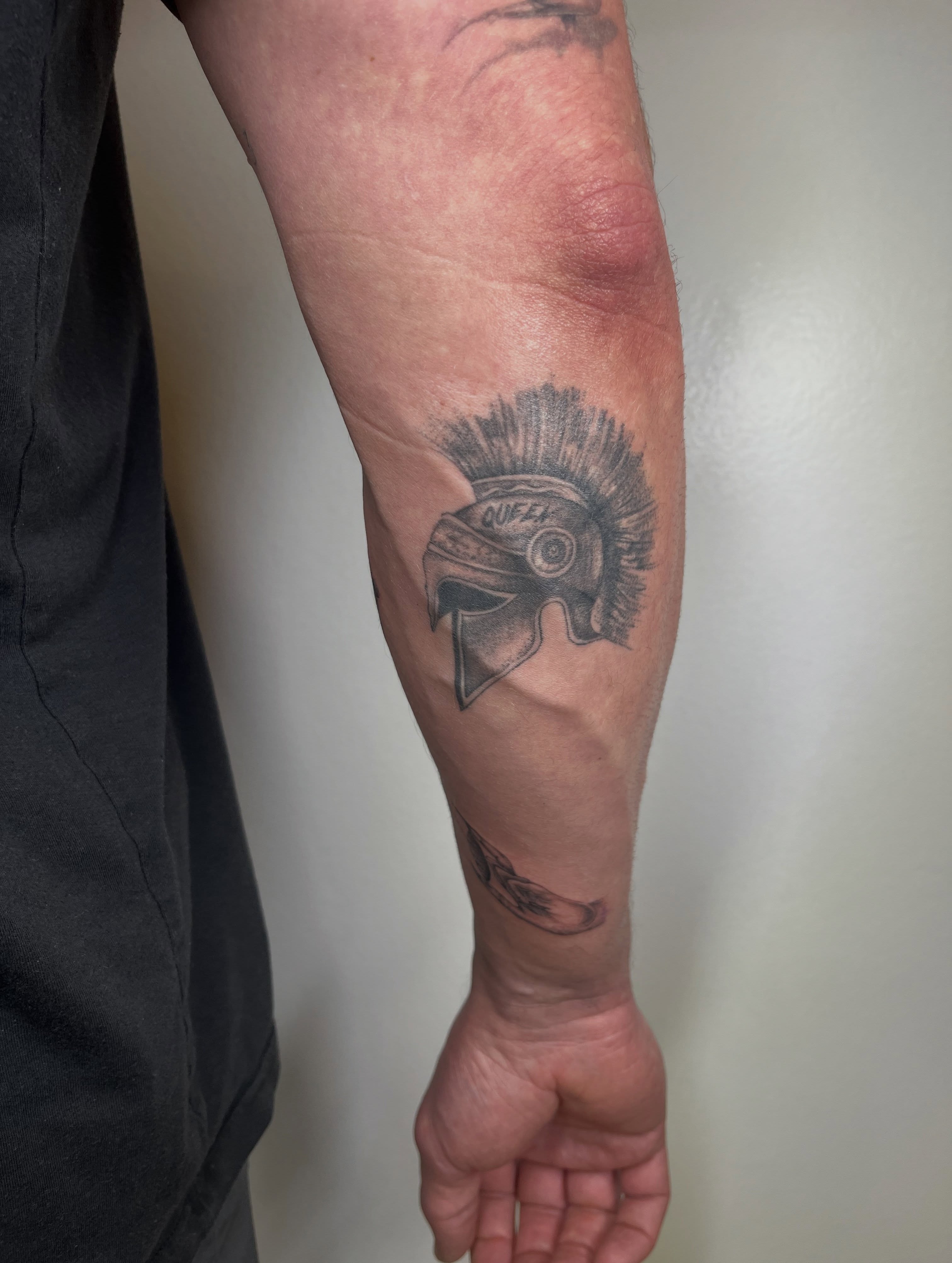 Spartan helmet black and grey tattoo on the forearm by kt