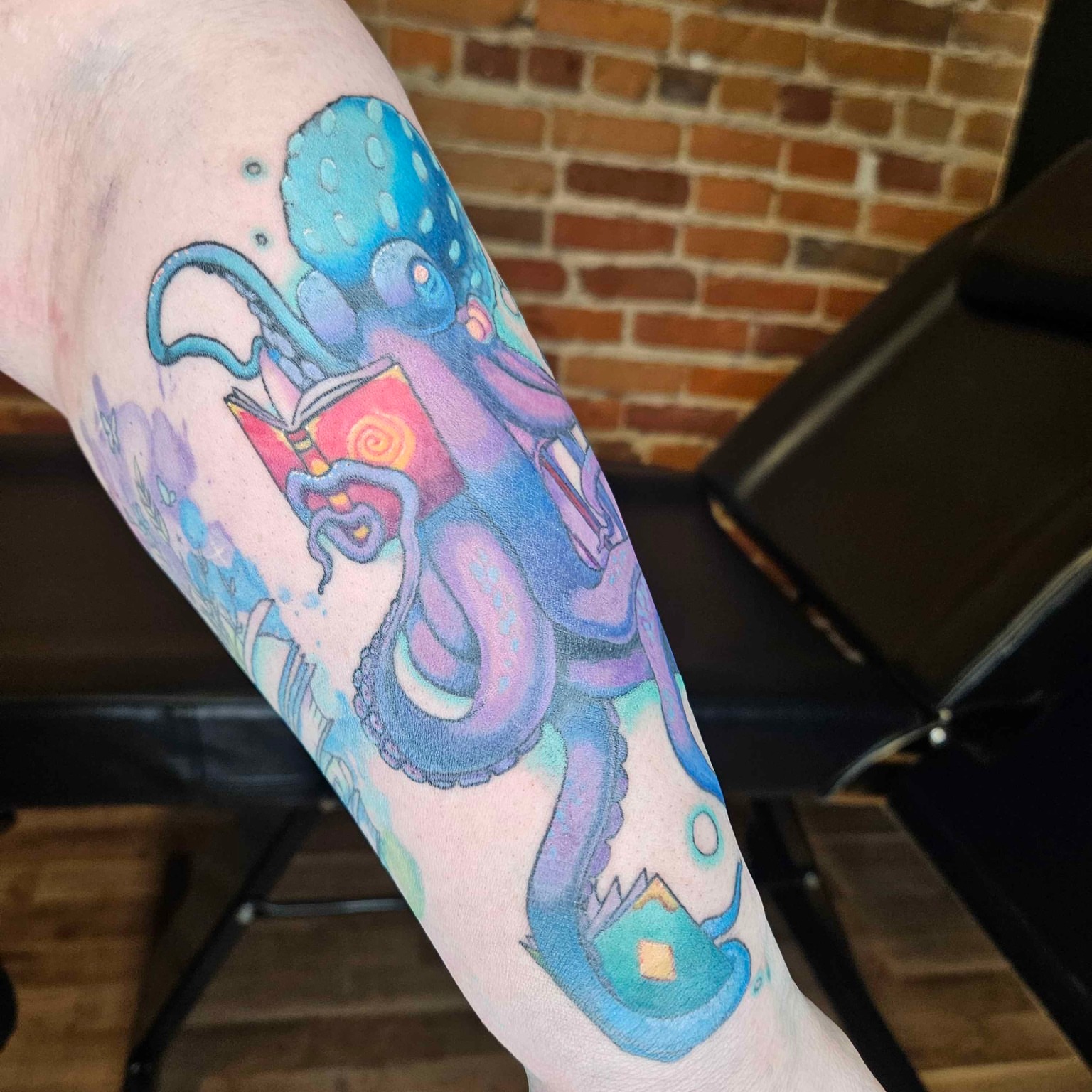 Octopus reading book watercolor tattoo on the forearm by Iram Withencroft
