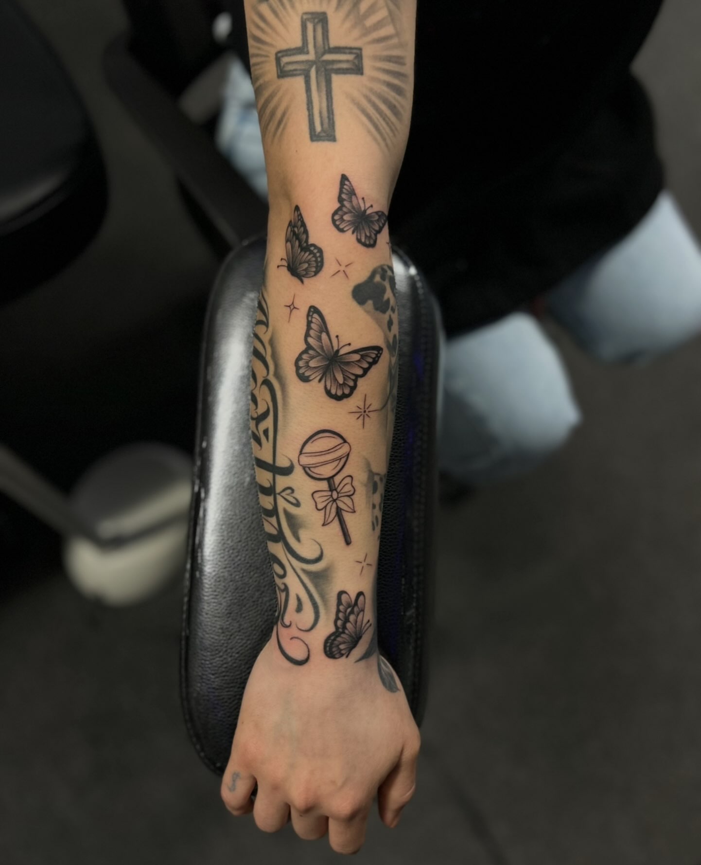 Butterflies and cross black and grey tattoo on the forearm by Tattoo Artist