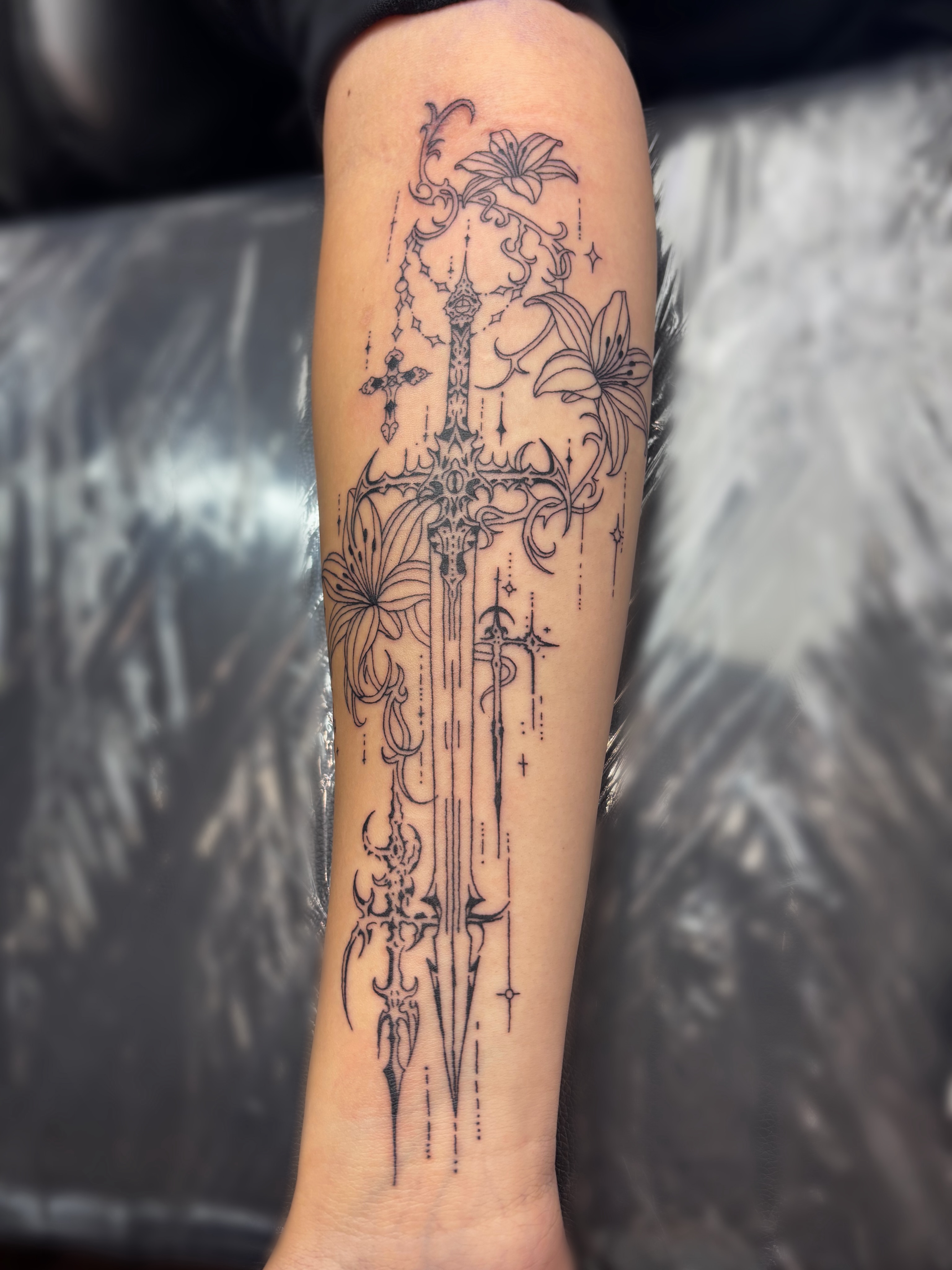 Cross and lilies ornamental tattoo on the forearm by Bree Burgess