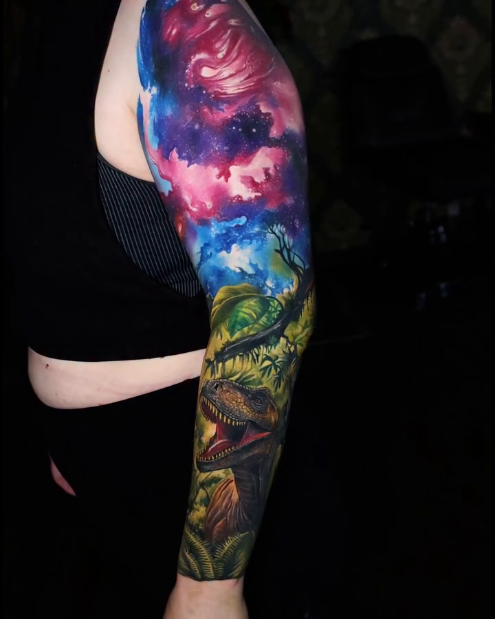 Cosmic landscape with dinosaurs watercolor tattoo on the upper arm by Marek Pawlik
