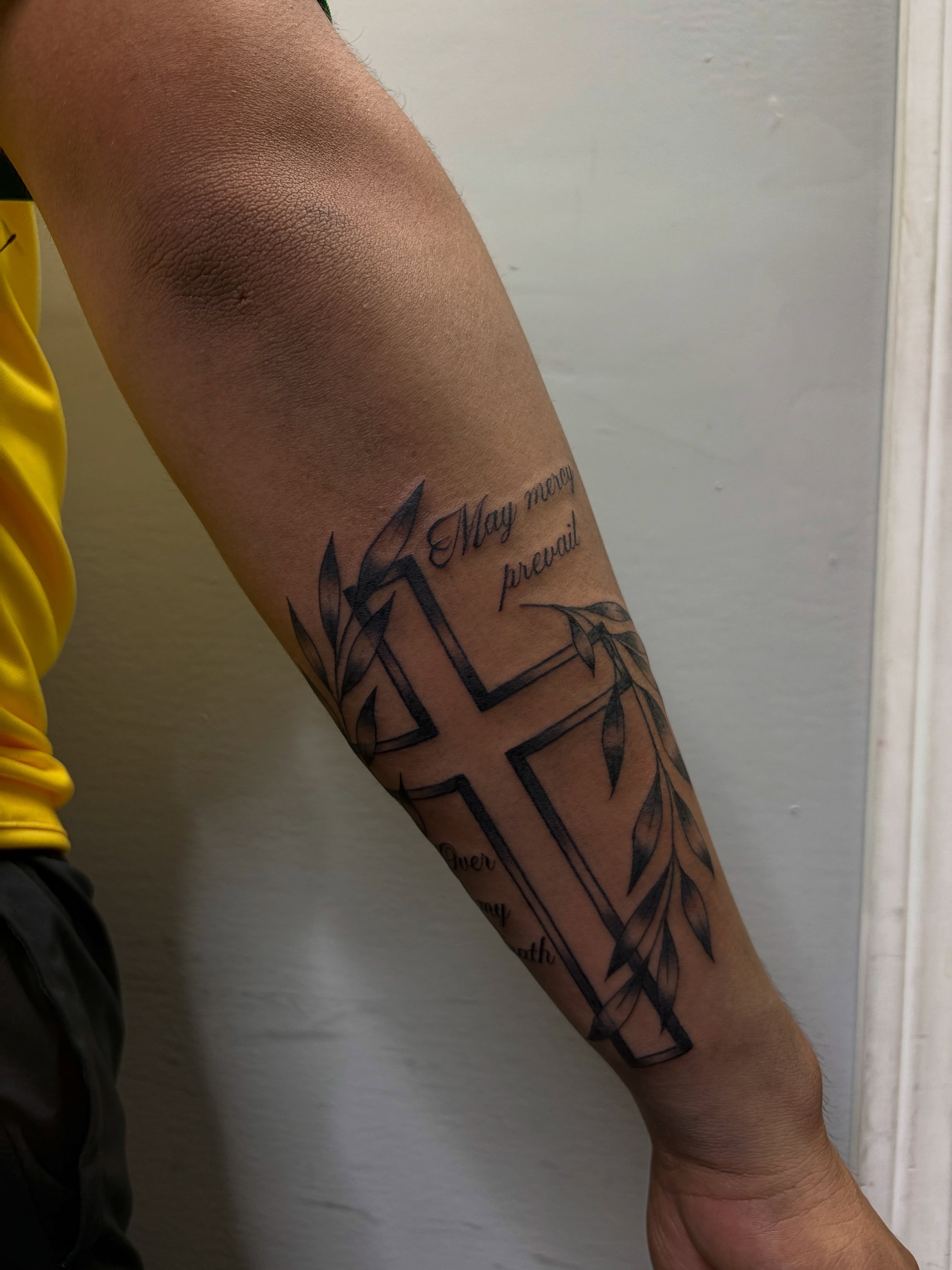 Cross with leaves black and grey tattoo on the forearm by Destineé