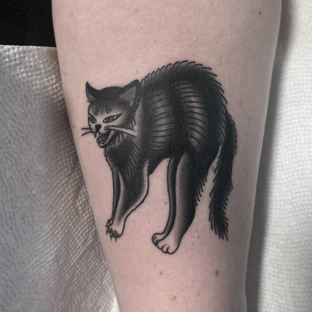 Angry cat black and grey tattoo on the forearm by Caeli Martin