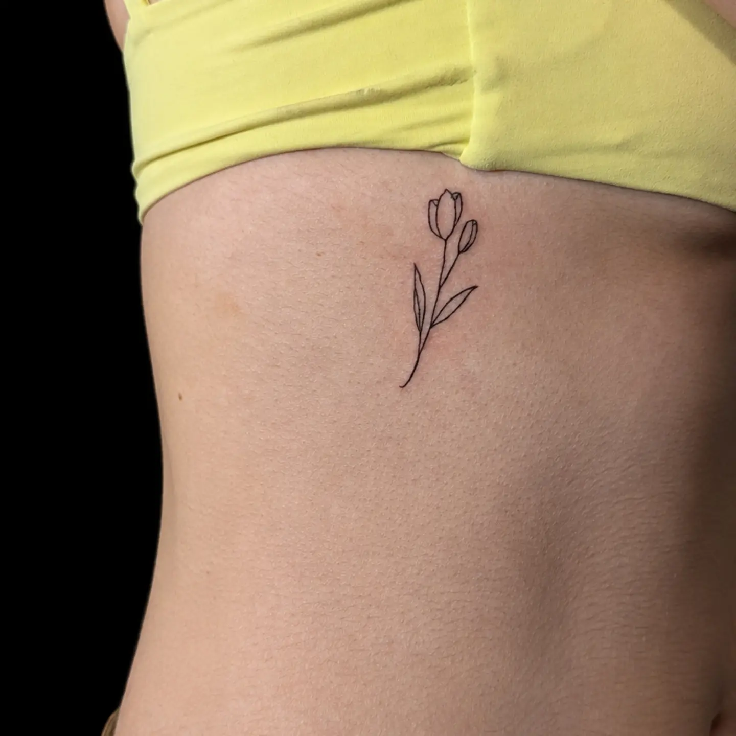 Tulip fine line tattoo on the ribs by Tony