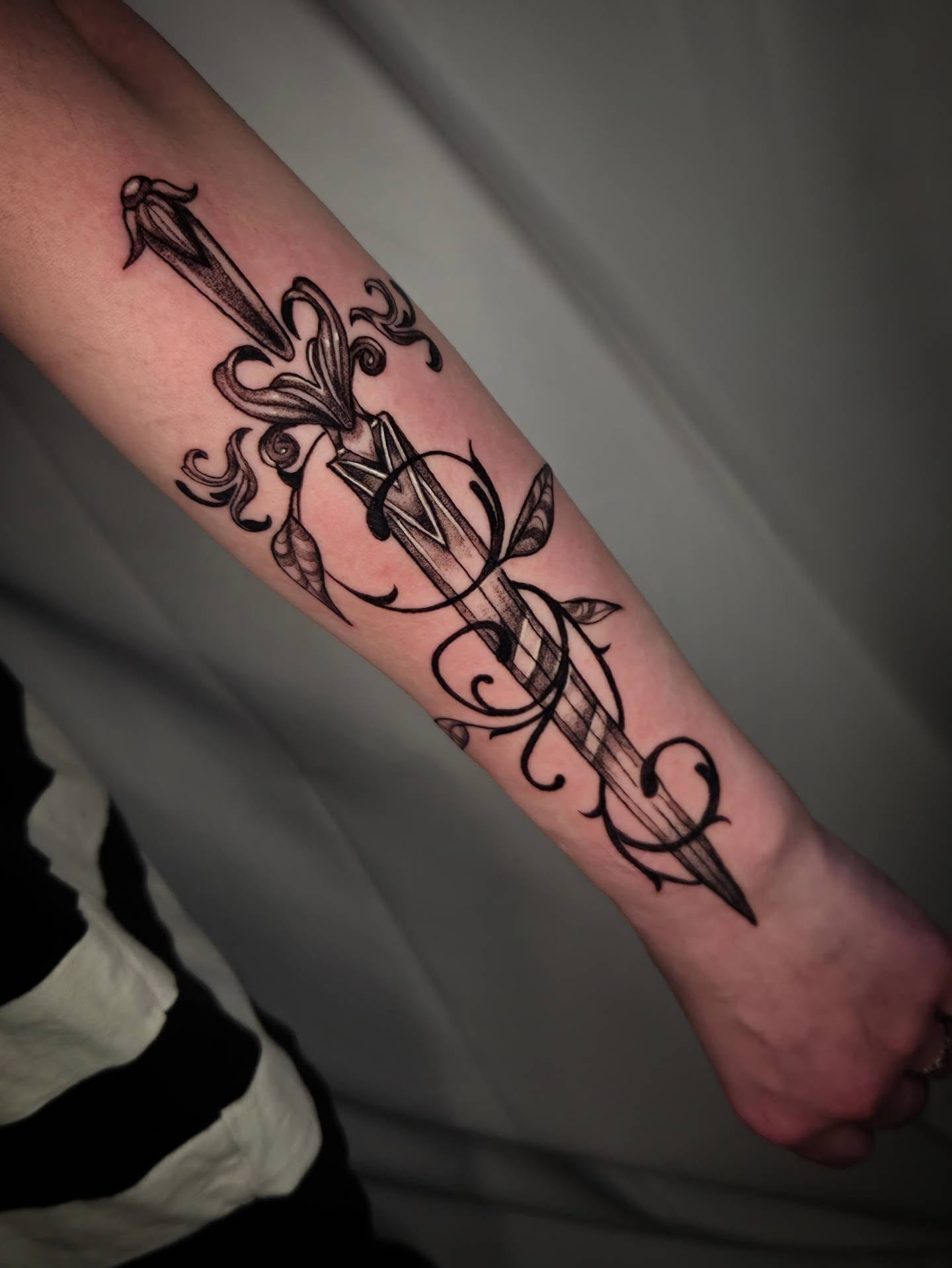 Sword and floral black and grey tattoo on the forearm by Devin 🖤