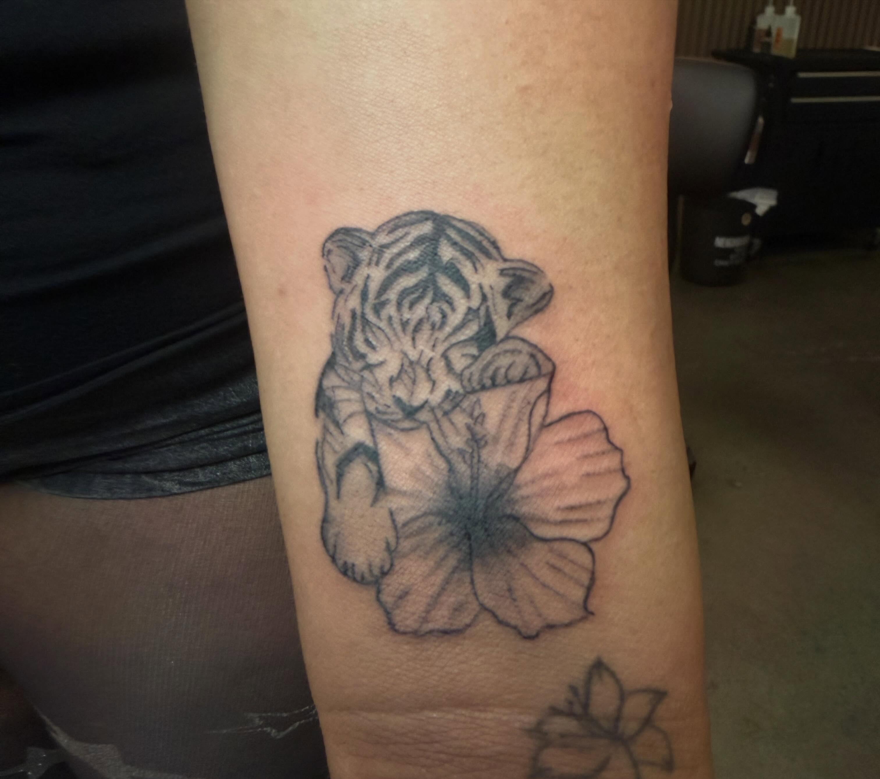 Tiger and hibiscus black and grey tattoo on the forearm by Lxx.