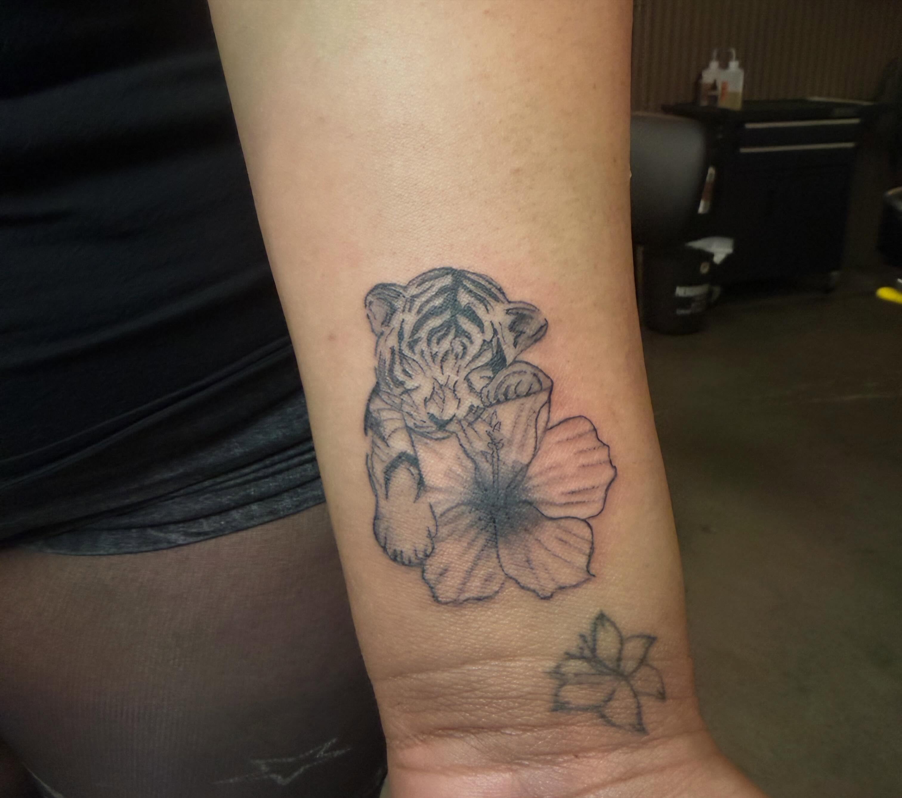 Tiger cub and flower black and grey tattoo on the forearm by Lxx.