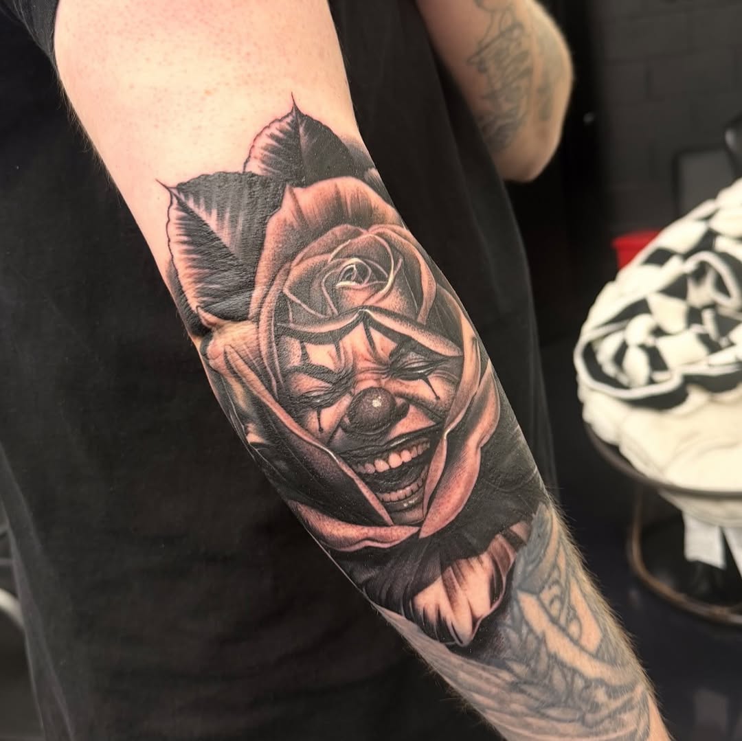 Clown face in a rose realism tattoo on the forearm by Dillinger, Ventura, California
