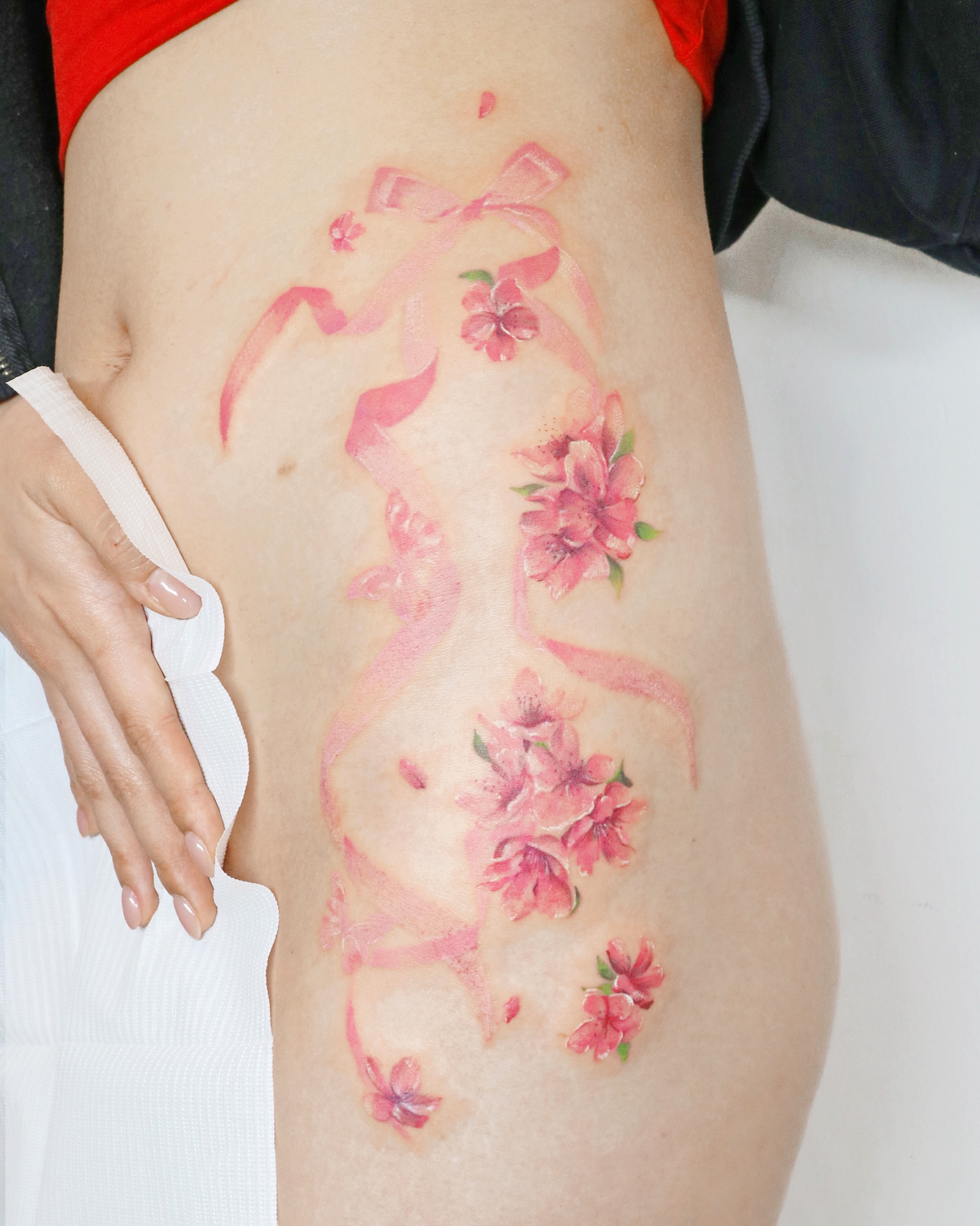 Cherry blossoms and ribbons watercolor tattoo on the thigh by Aroha