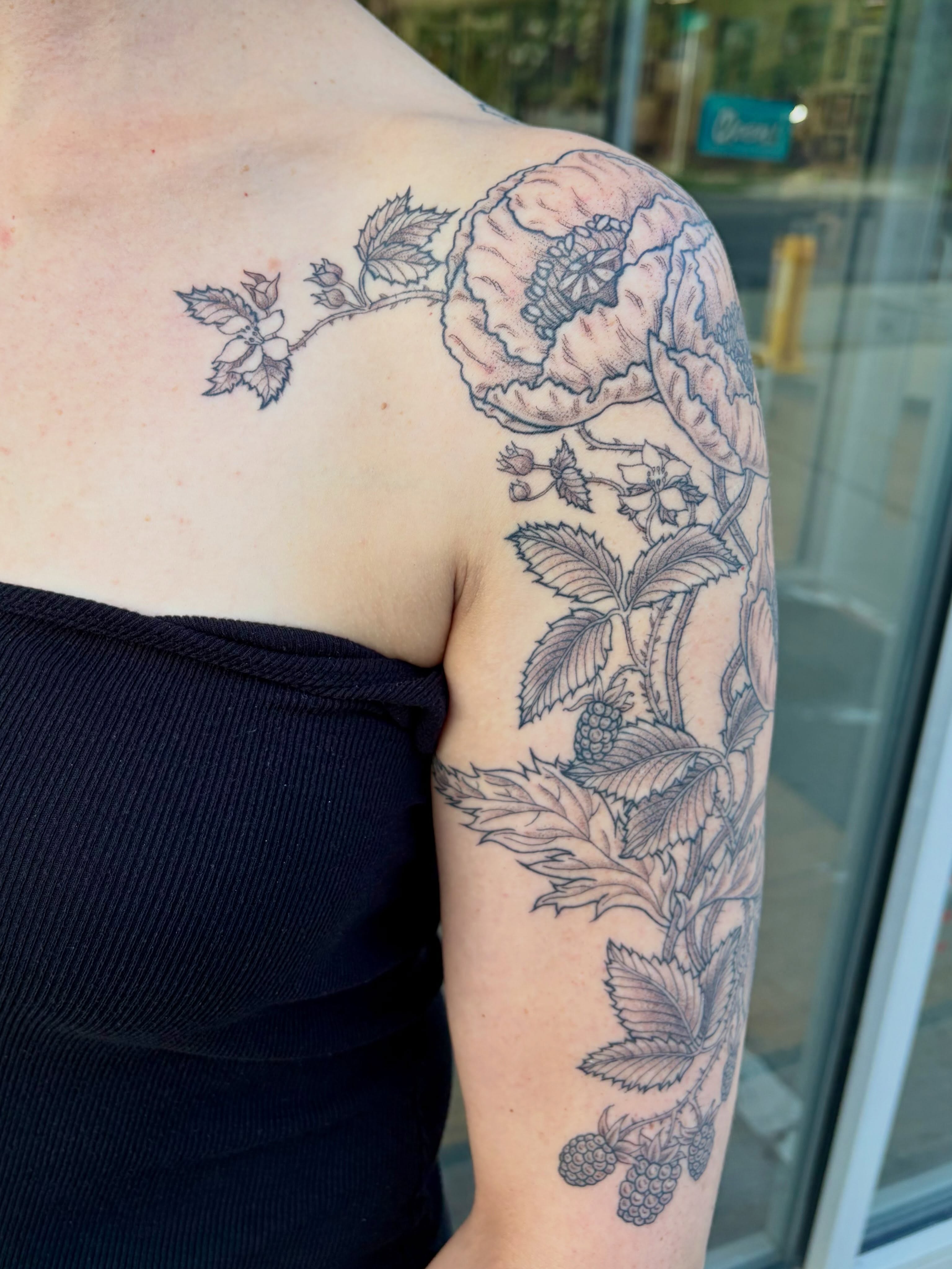 Flower and leaves black and grey tattoo on the upper arm by Sarah Roach
