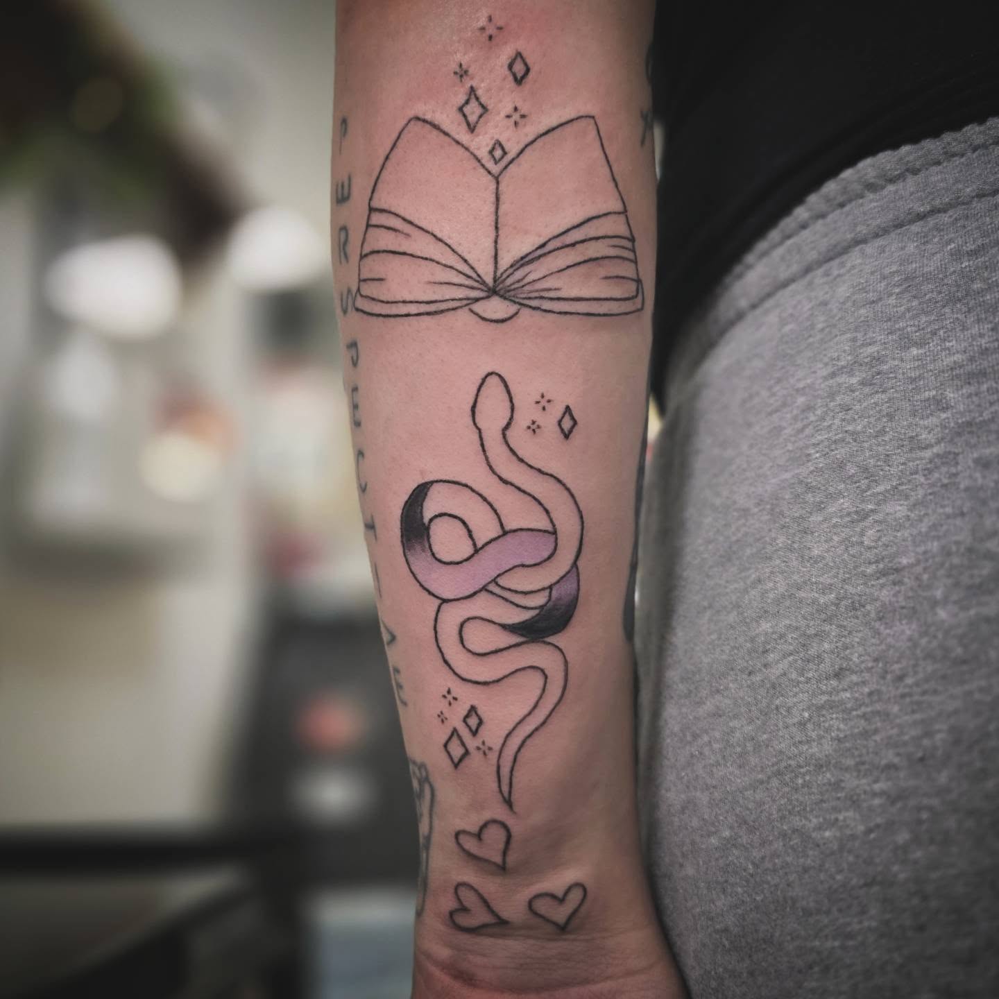 Book and snake fine line tattoo on the forearm by Anntonietta Borzacchiello