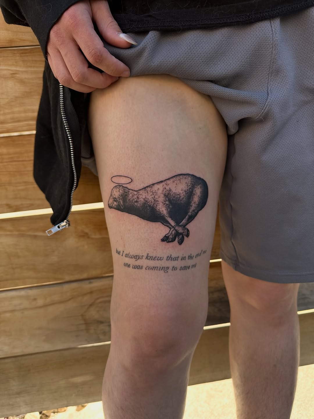 Lamb with halo and text fine line tattoo on the thigh by 𝓡𝓸𝓼𝓮 𝓗𝓪𝔂𝓮𝓼