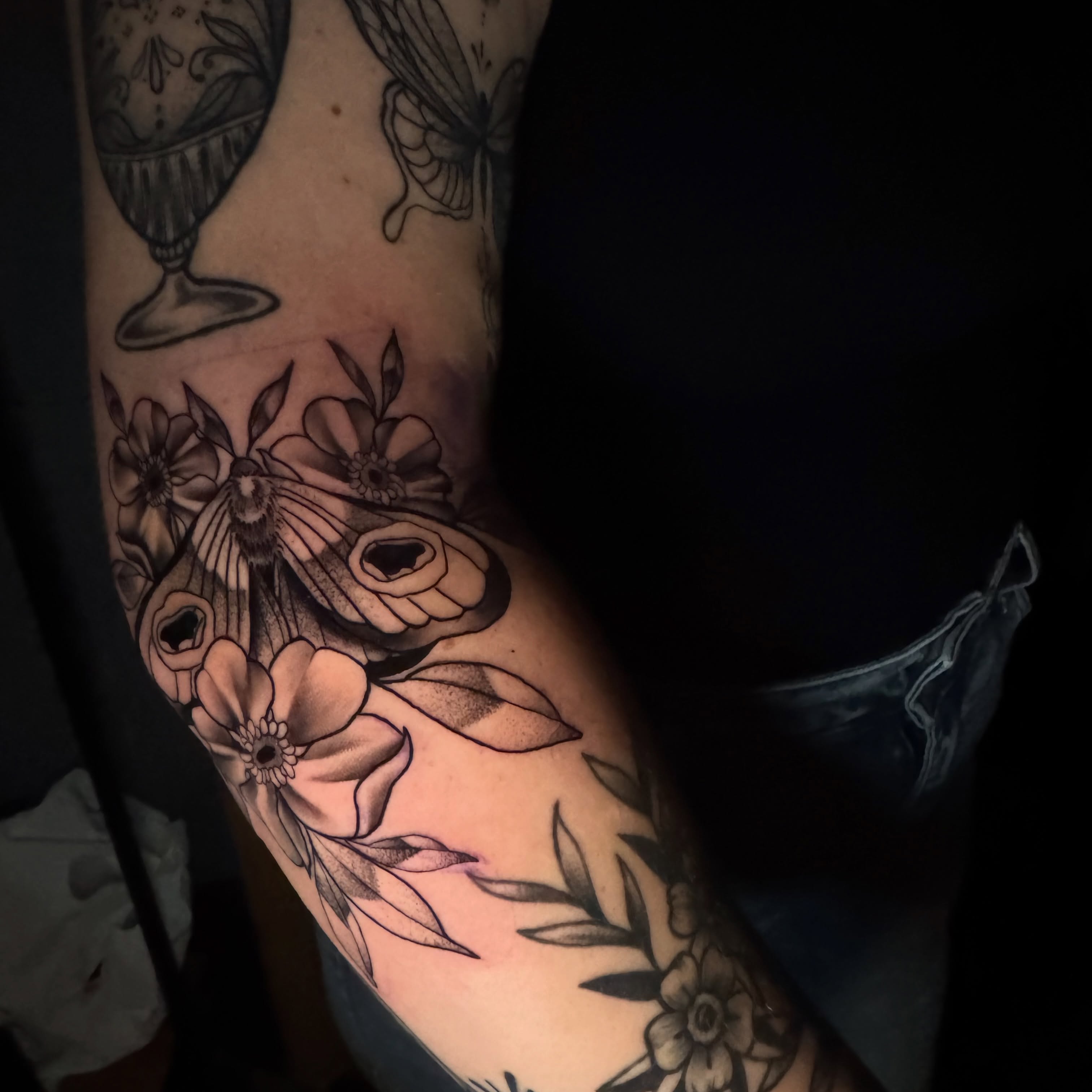 Flowers and moth black and grey tattoo on the forearm by tori 🫶🏻