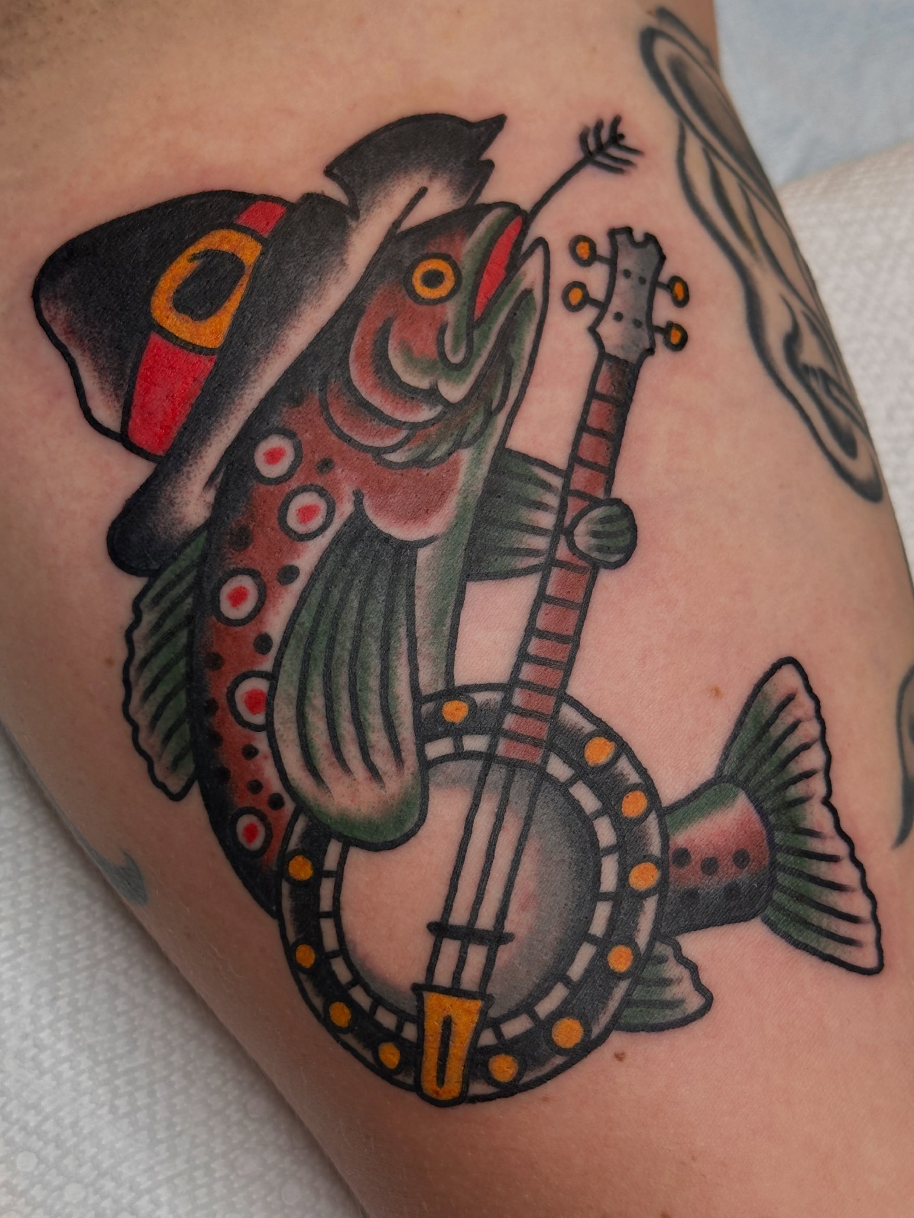 Fish playing banjo American traditional tattoo on the upper arm by Cody Woolard, Seymour, Tennessee
