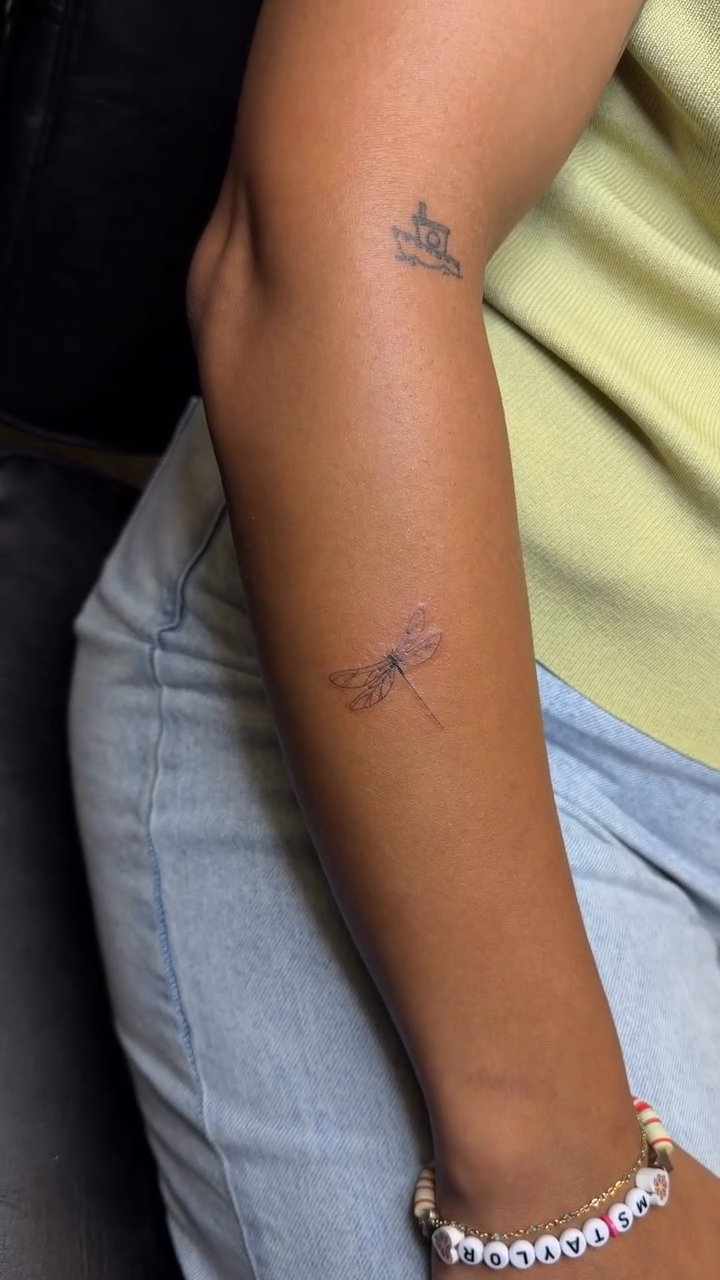 Dragonfly and script text fine line tattoo on the upper arm by Pretty Ugly Tattoos