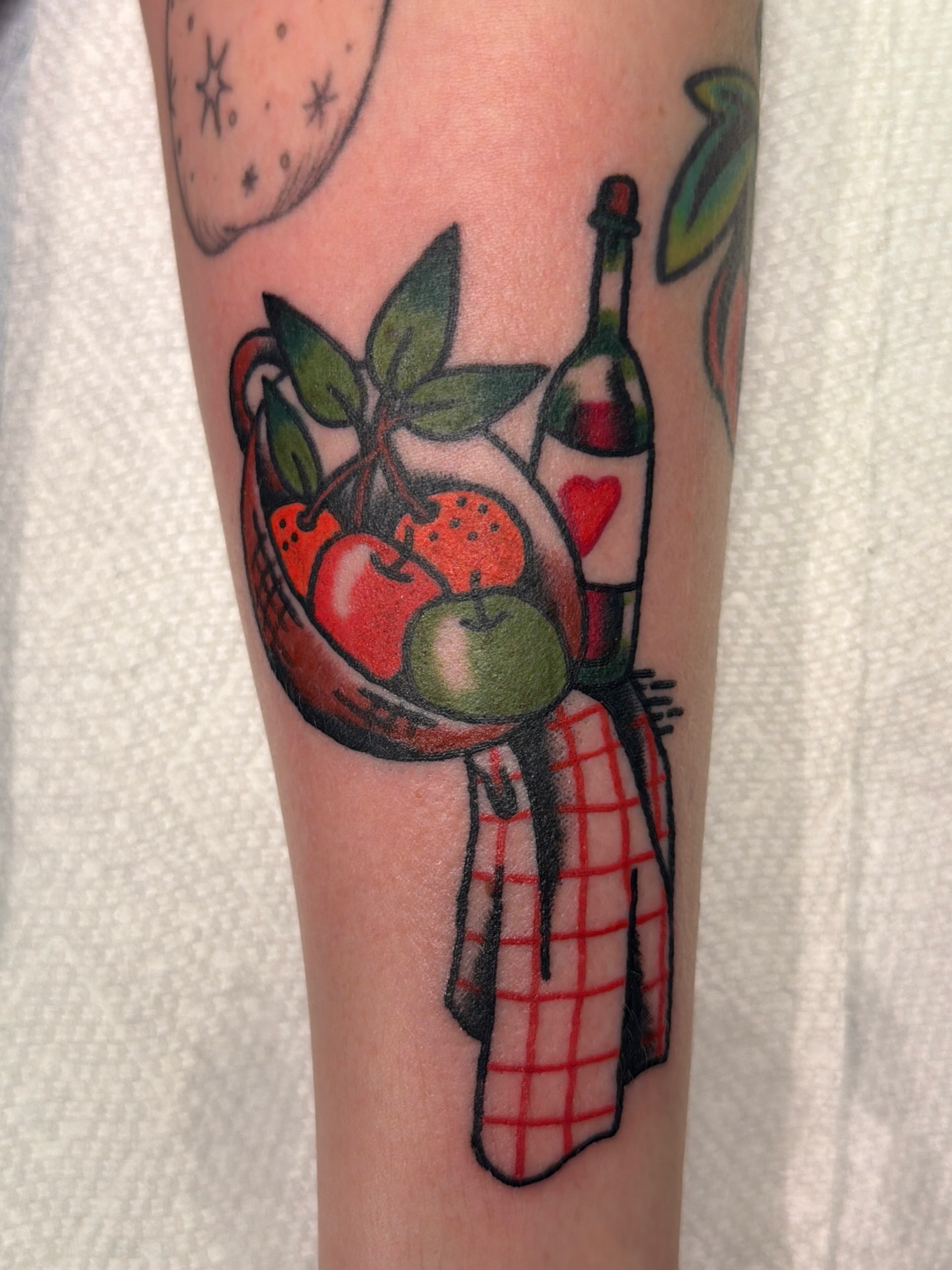 Basket of fruit and wine bottle American traditional tattoo on the forearm by Emma Fox Tattoo