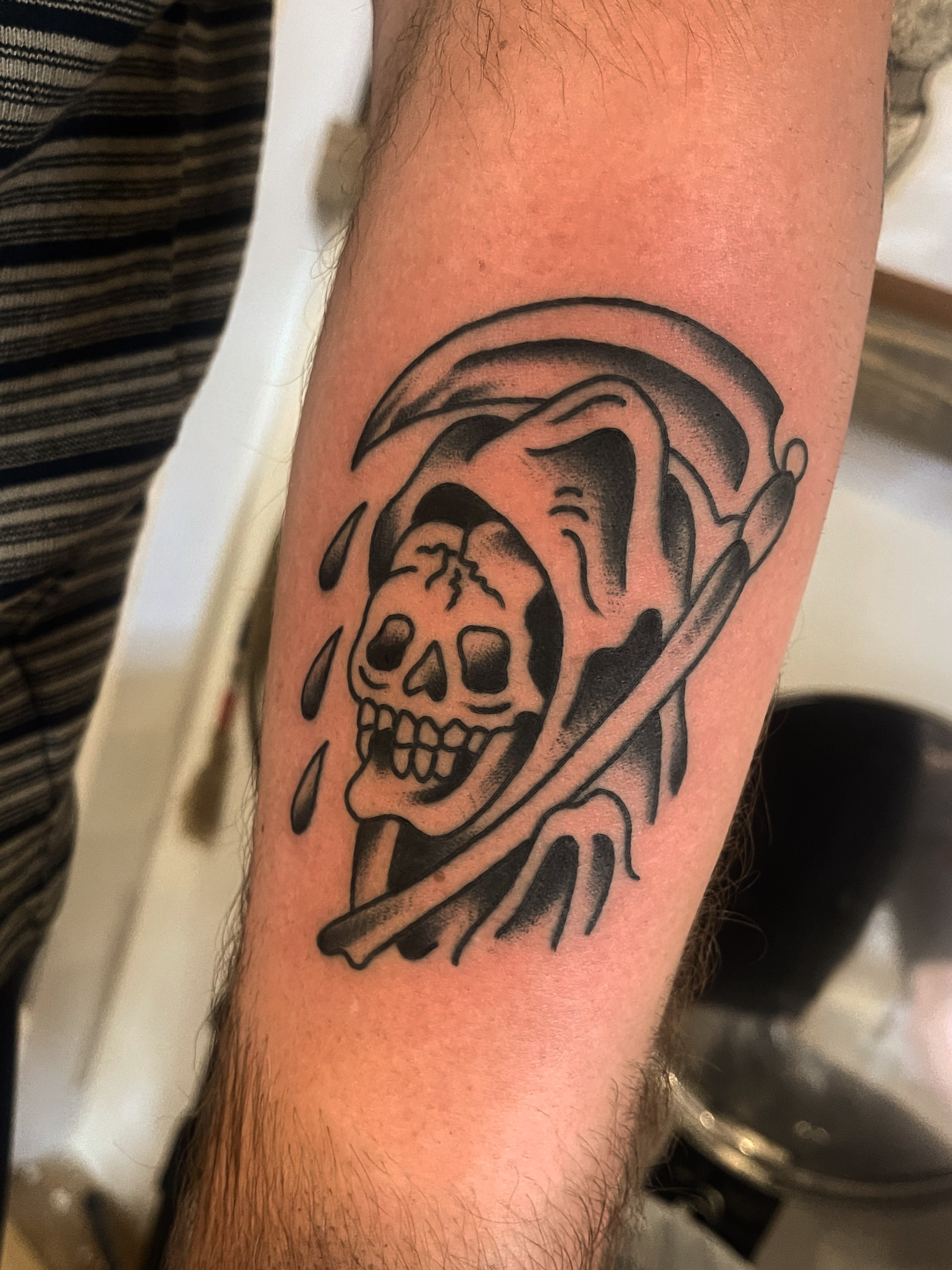 Skull with scythe American traditional tattoo on the forearm by Spencer Reisbeck