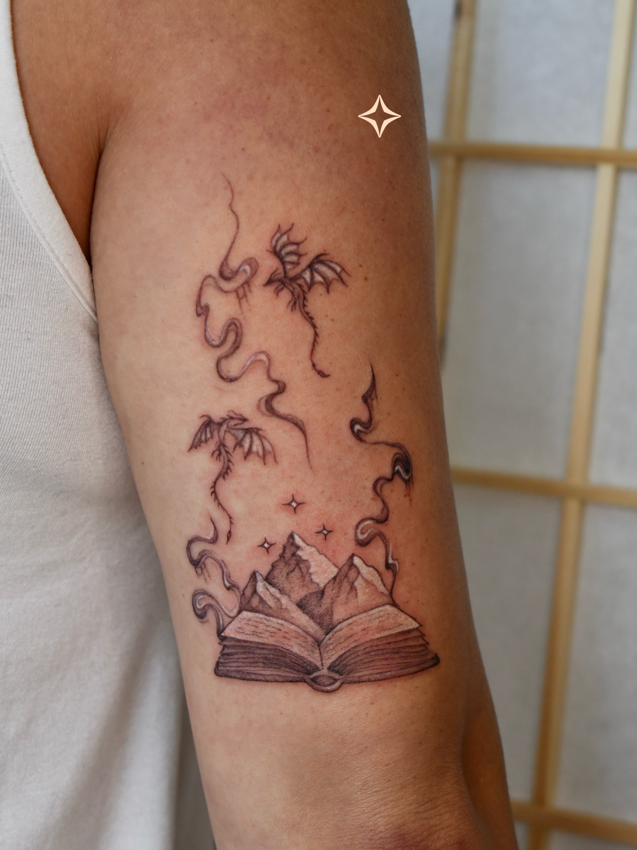 Open book with mountains and dragon dotwork tattoo on the forearm by 𝐇𝐚𝐫𝐩𝐞𝐫