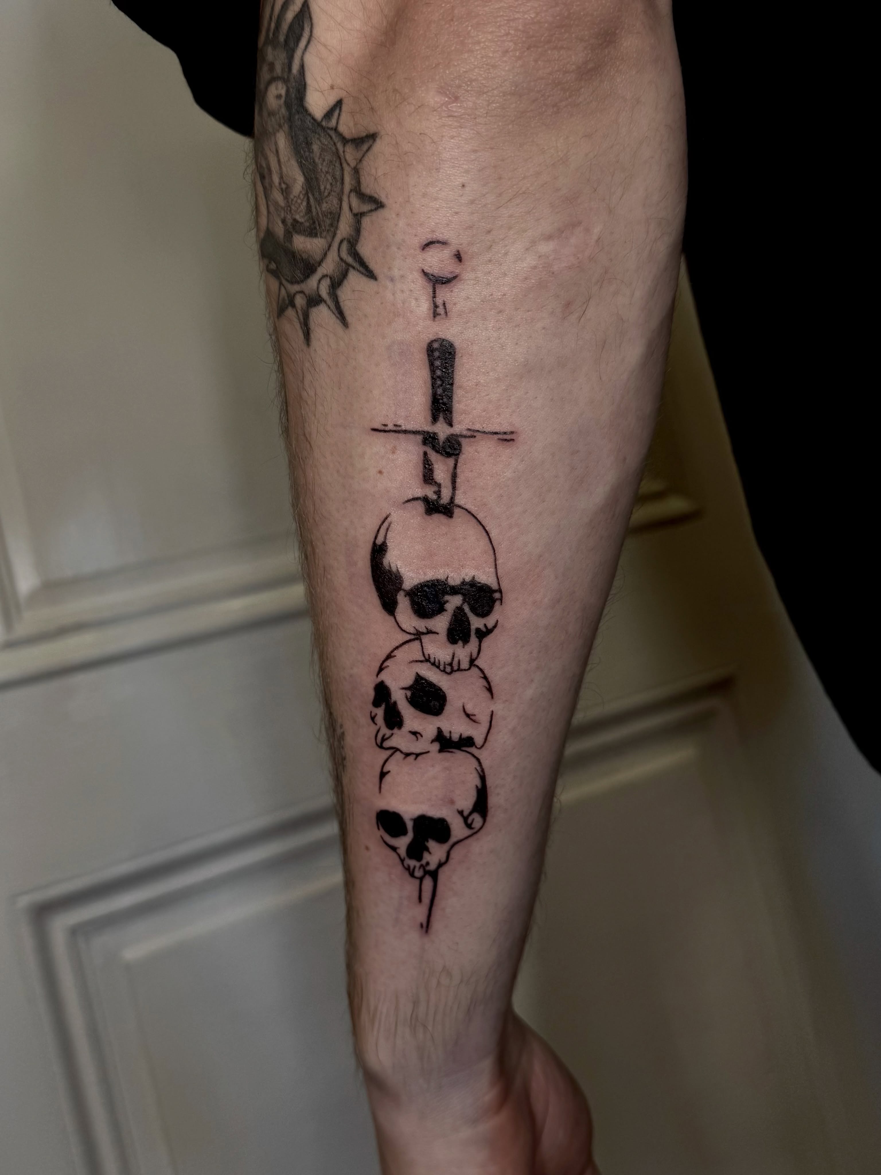 Skulls and dagger black and grey tattoo on the forearm by Ian Saner