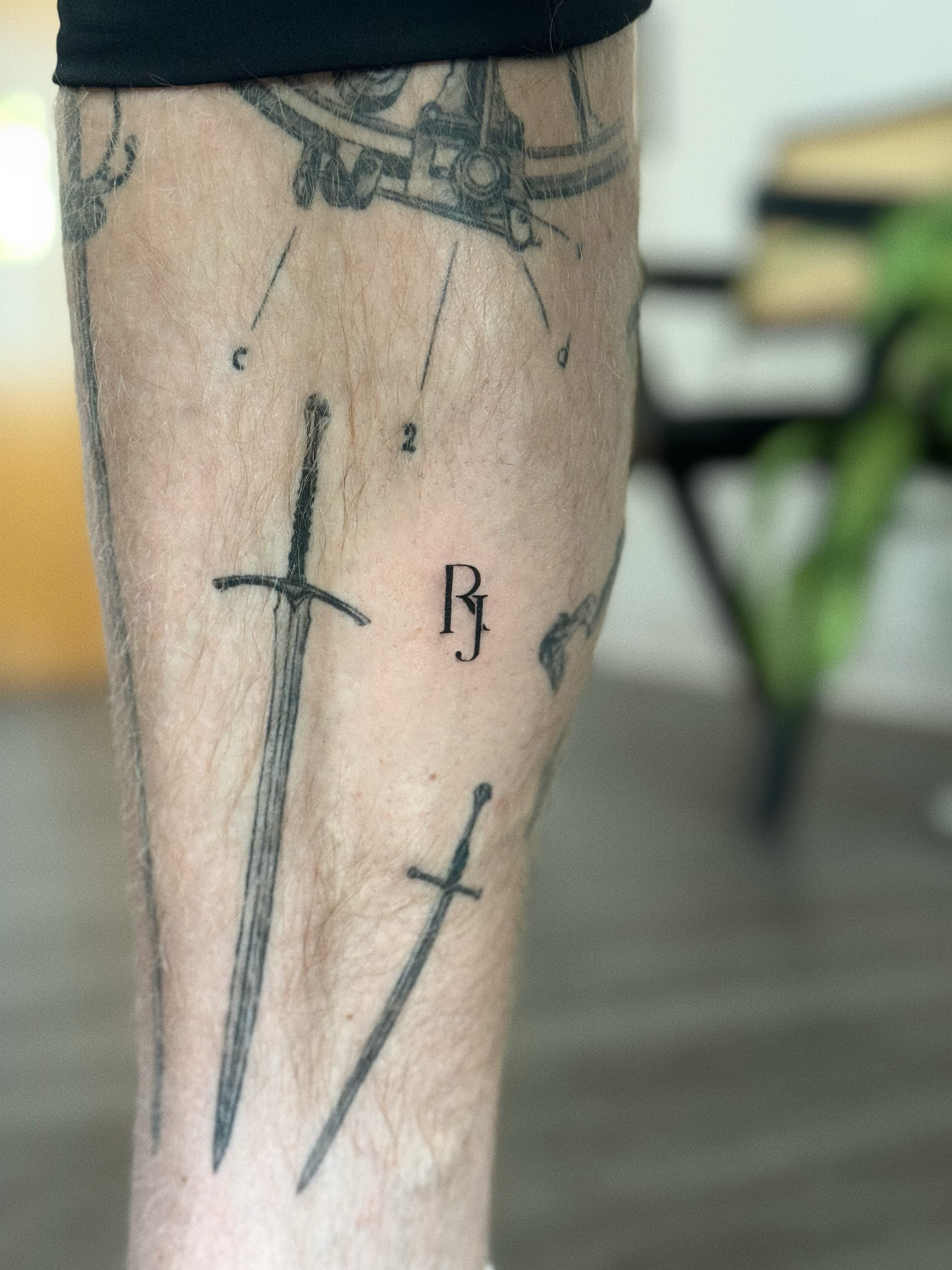 Sword and initials black and grey tattoo on the forearm by Victoria