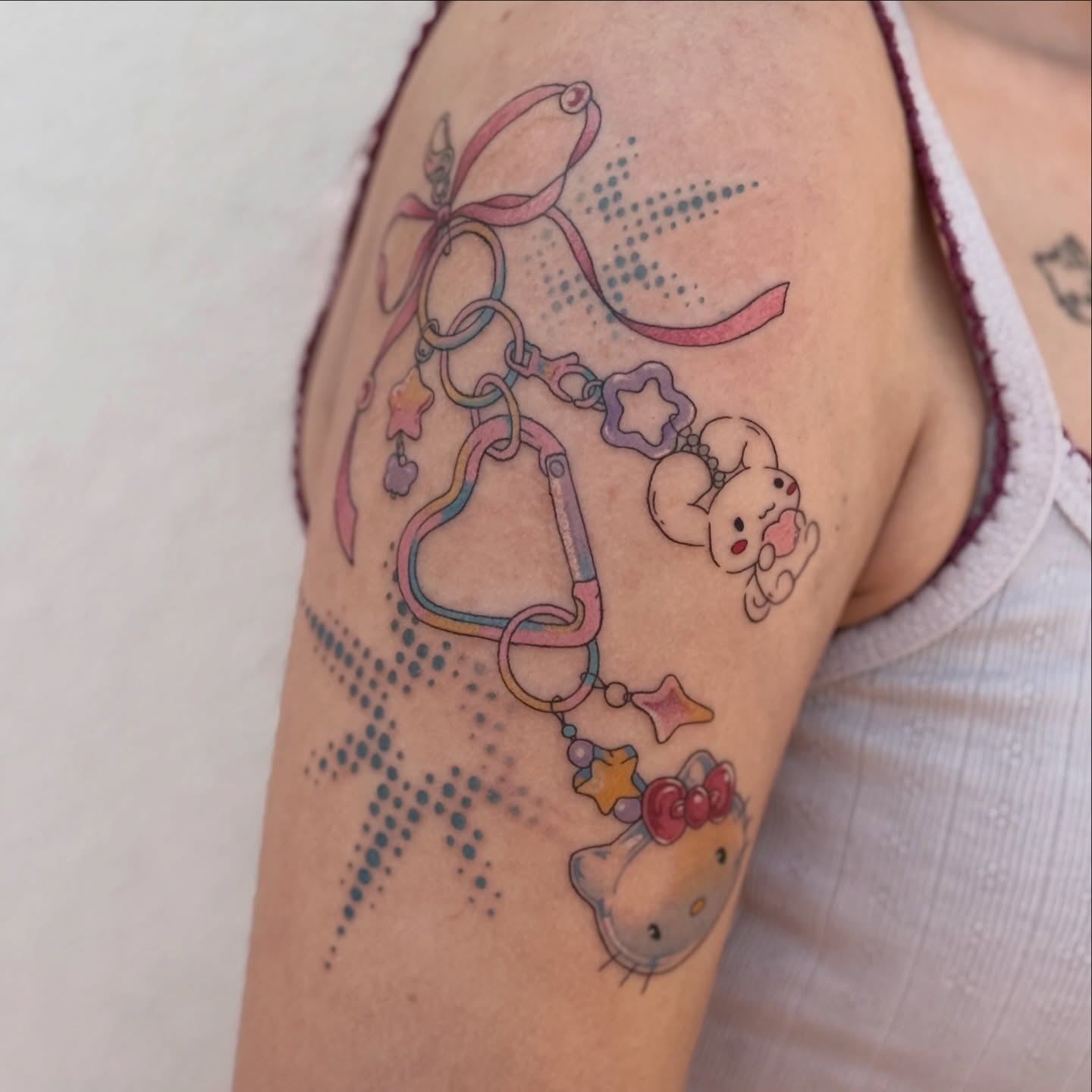 Hello Kitty accessories dotwork tattoo on the upper arm by Jordan