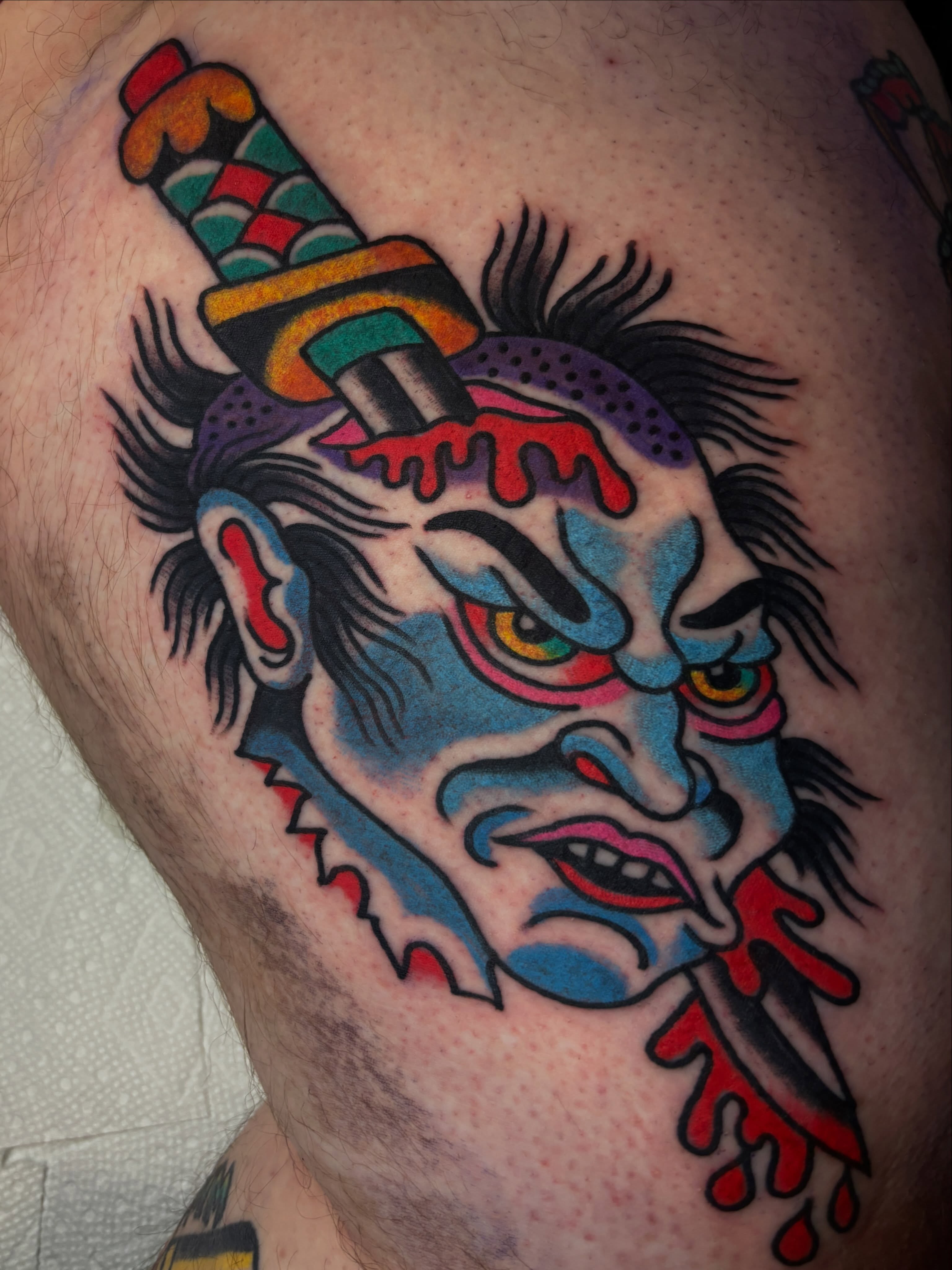 Clown head with knife American traditional tattoo on the thigh by Mitch Ashpaugh